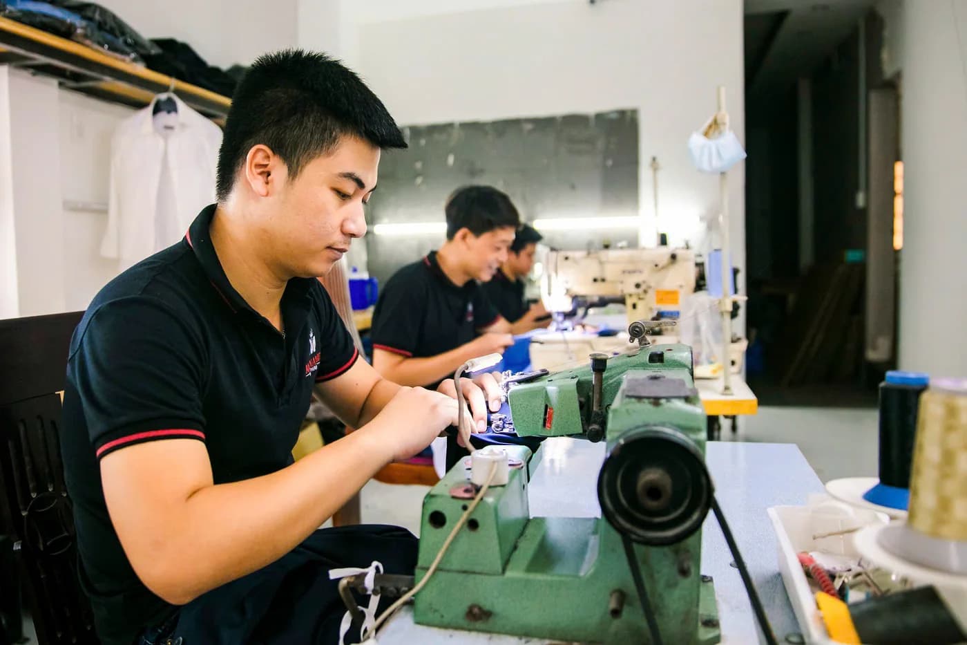 Thợ trẻ áo polo đen may trên máy chuyên dụng xanh