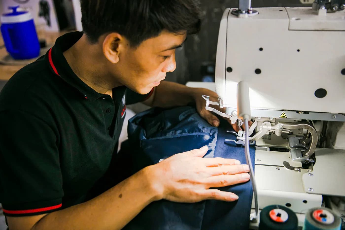 Thợ trẻ áo polo đen chăm chú may thân vest xanh navy