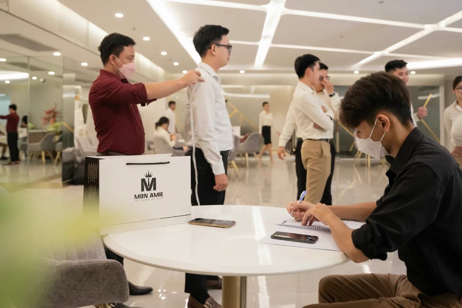 Đo vai cho nhân viên nam giữa sảnh, đồng nghiệp chờ phía sau