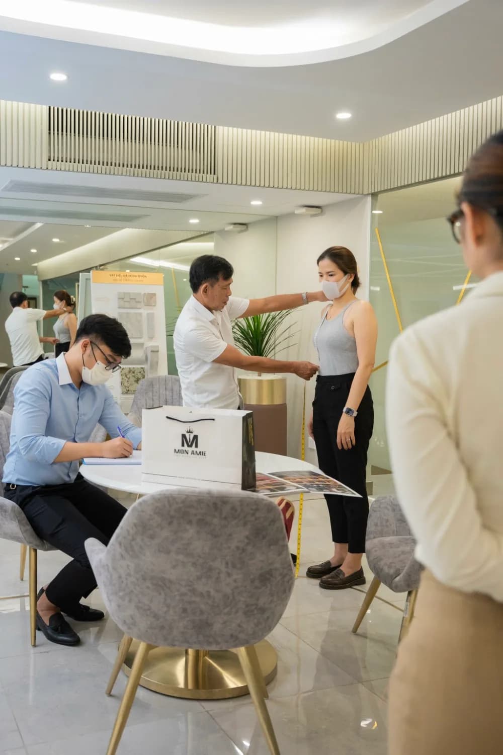 Đo vòng eo cho nhân viên nữ, thợ ghi phiếu bên bàn