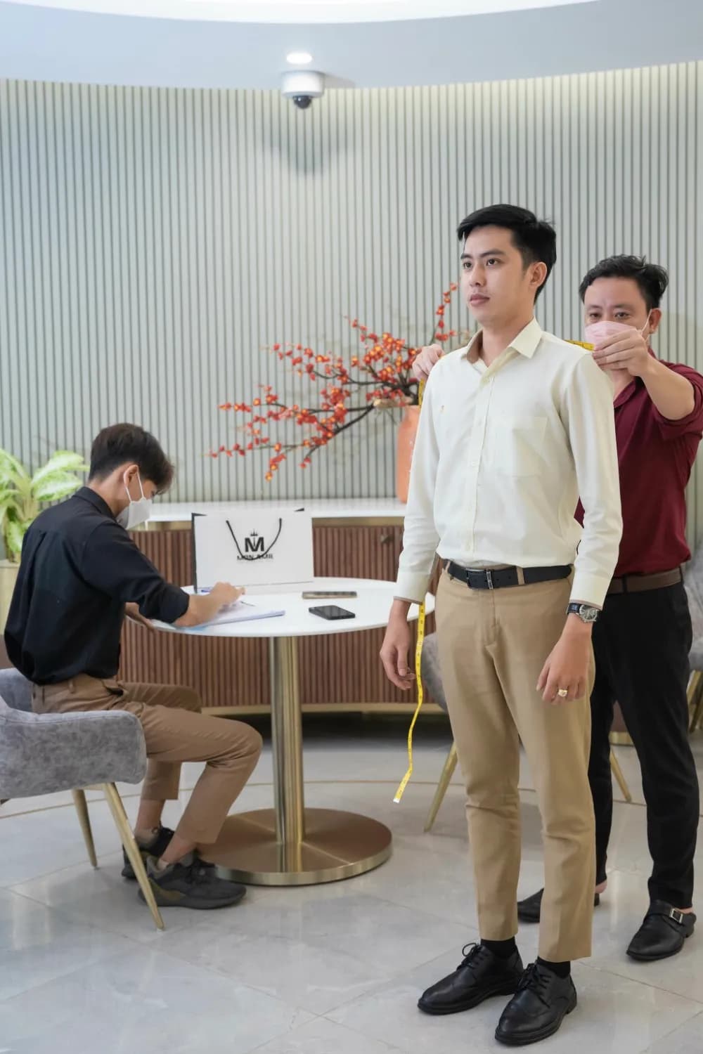 Khách nam sơ mi trắng quần kaki đứng đo số đo toàn thân tại phòng chờ sang trọng