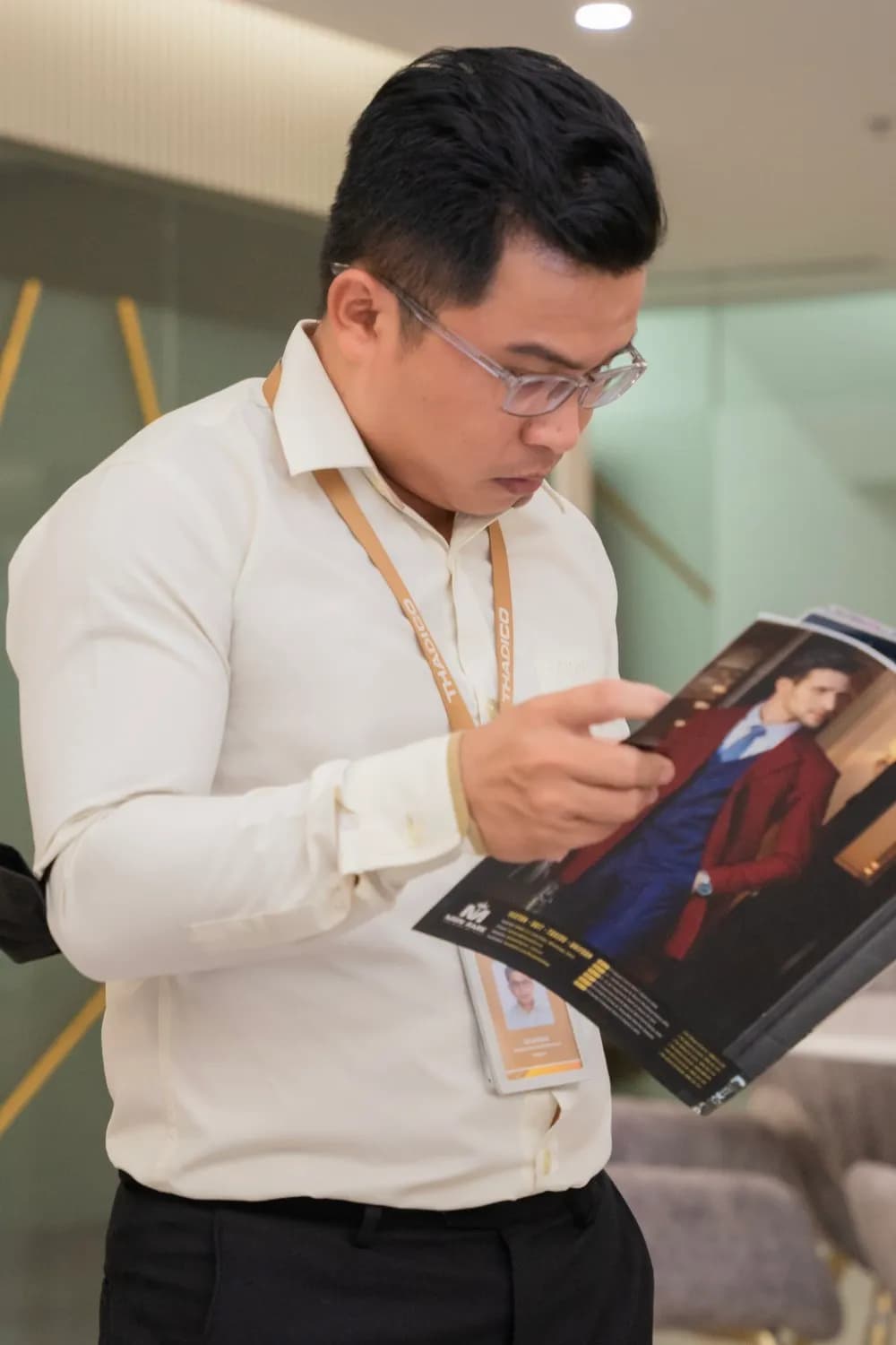 Khách nam sơ mi be chăm chú xem catalogue vest Mon Amie, ánh sáng ấm