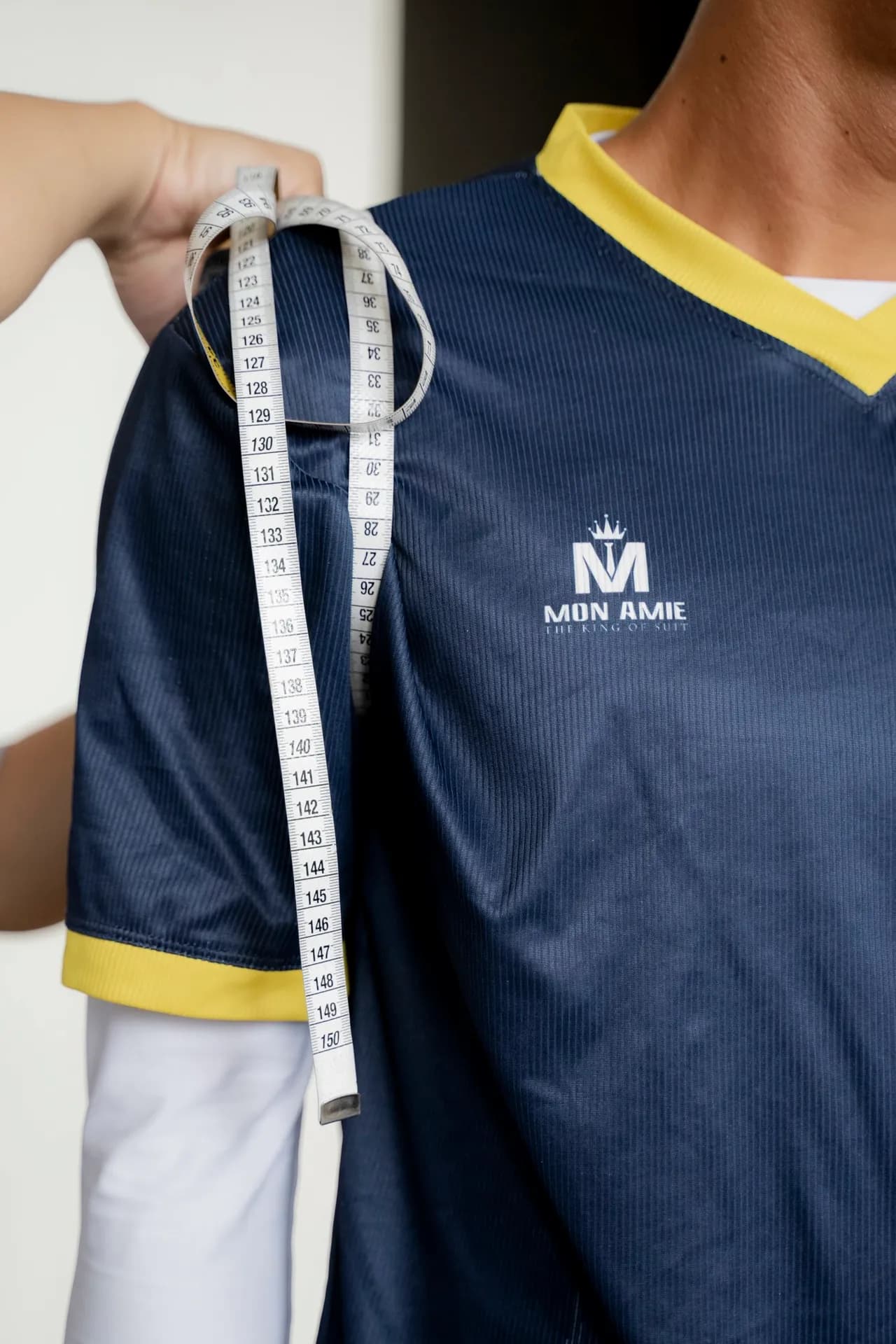 Cận cảnh thước dây đo vai áo thi đấu xanh navy viền vàng, logo Mon Amie trên ngực