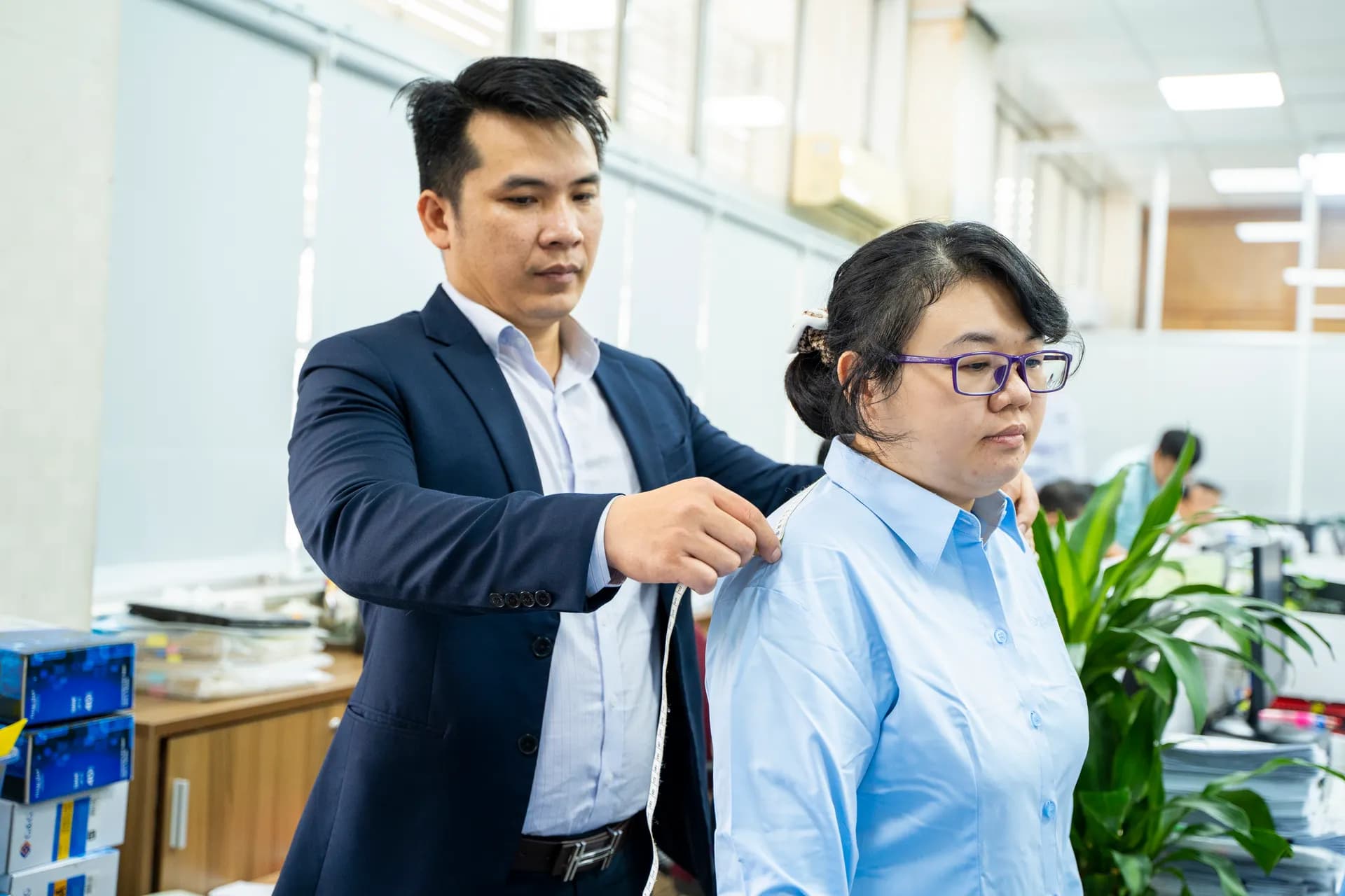 Thợ may vest navy chỉnh vai áo sơ mi xanh nhạt cho nhân viên nữ đeo kính