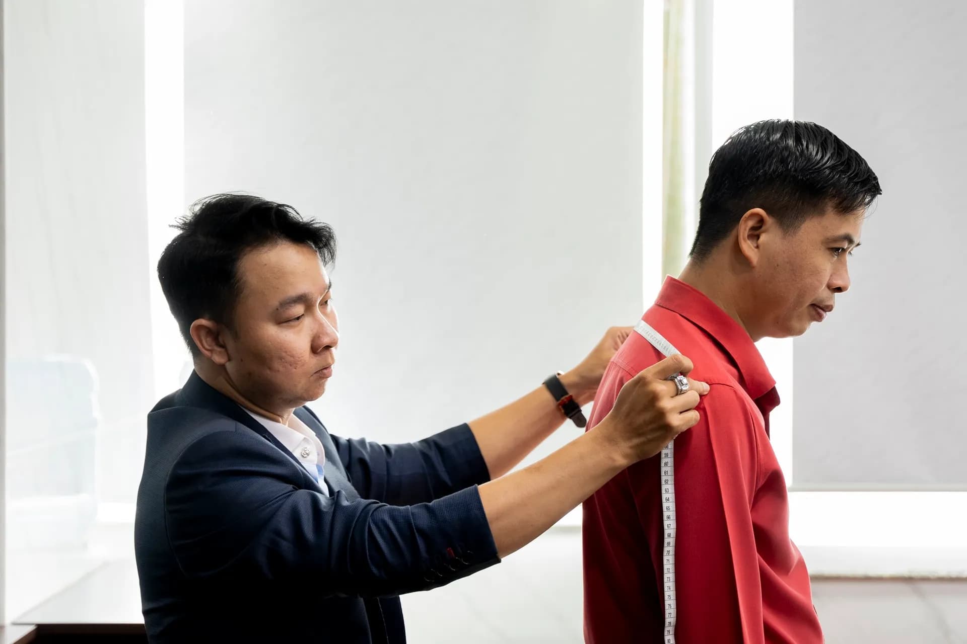 Đo tay áo cho khách mặc polo đỏ, ánh sáng cửa sổ tự nhiên