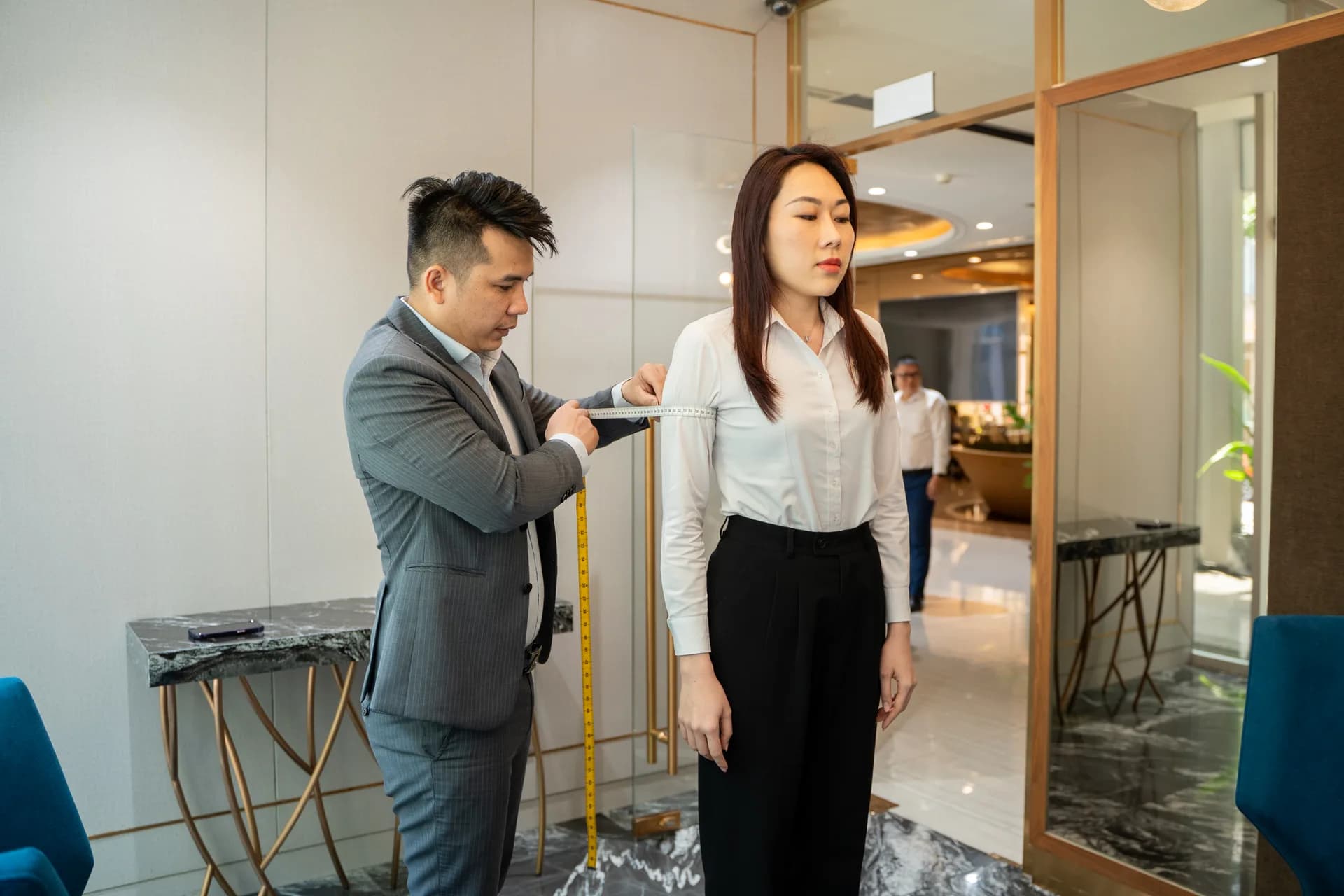 Đo chiều dài tay áo cho nhân viên nữ bên khung kính vàng đồng