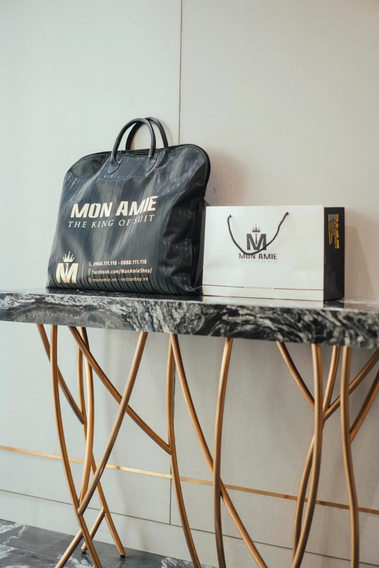 Túi đựng vest Mon Amie đen vàng cạnh túi giấy, bàn console chân vàng