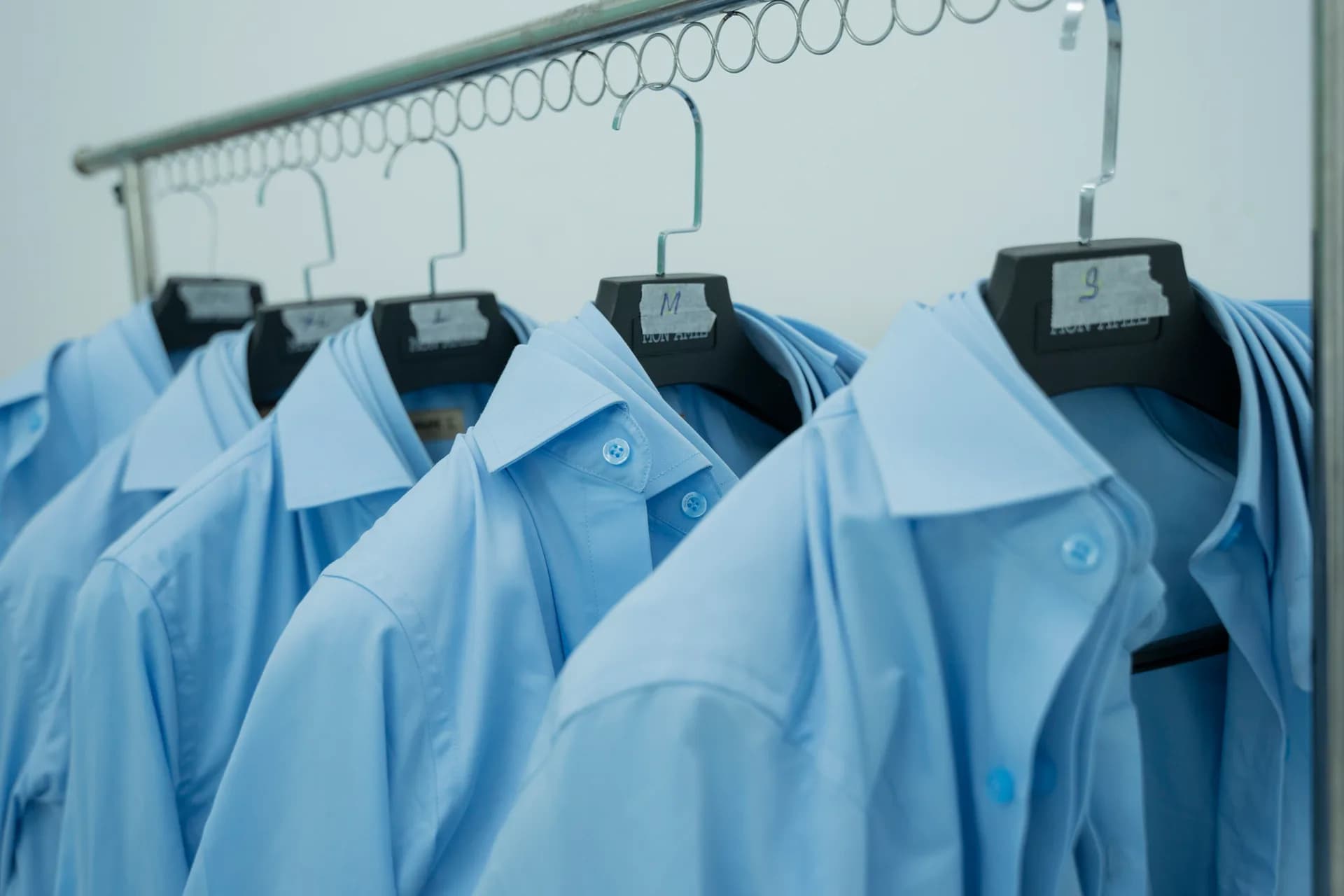 Áo sơ mi xanh mẫu gắn nhãn size S, M, L treo sẵn để nhân viên thử