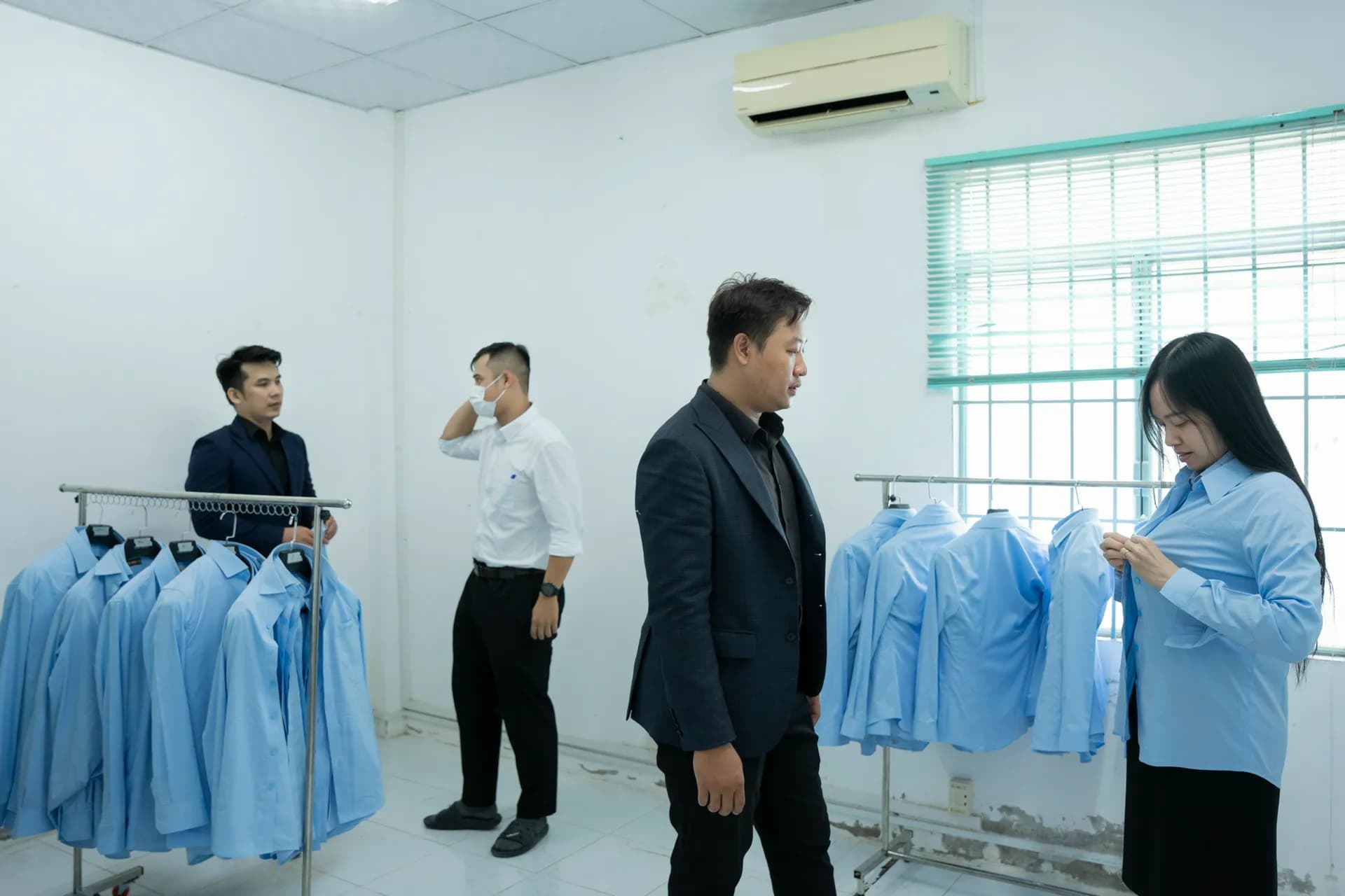Buổi thử áo sơ mi xanh nhạt đồng phục, dãy áo treo trên giá và nhân viên thử đồ
