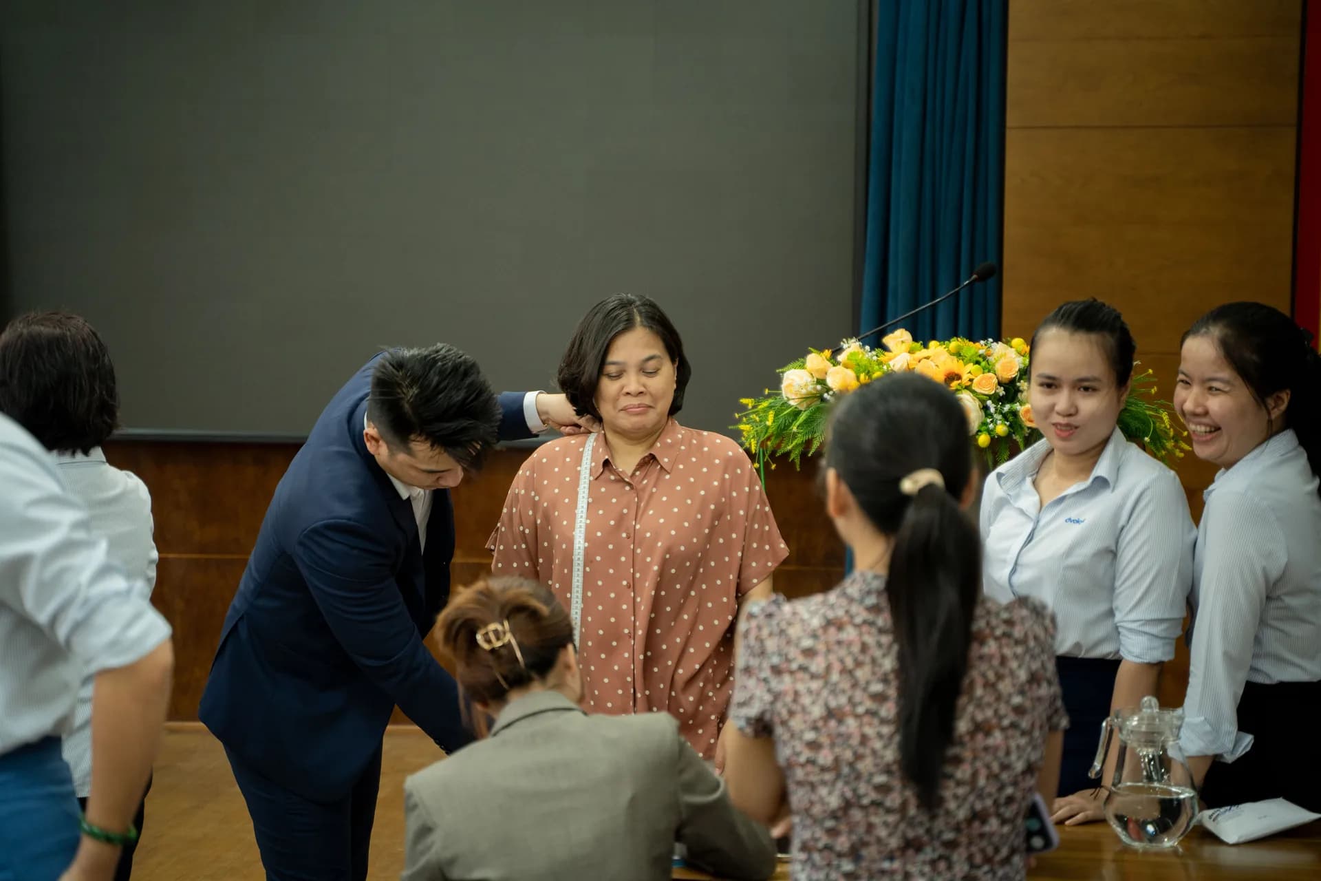 Đo vai cho nhân viên nữ, đồng nghiệp phía sau vui vẻ chờ đến lượt