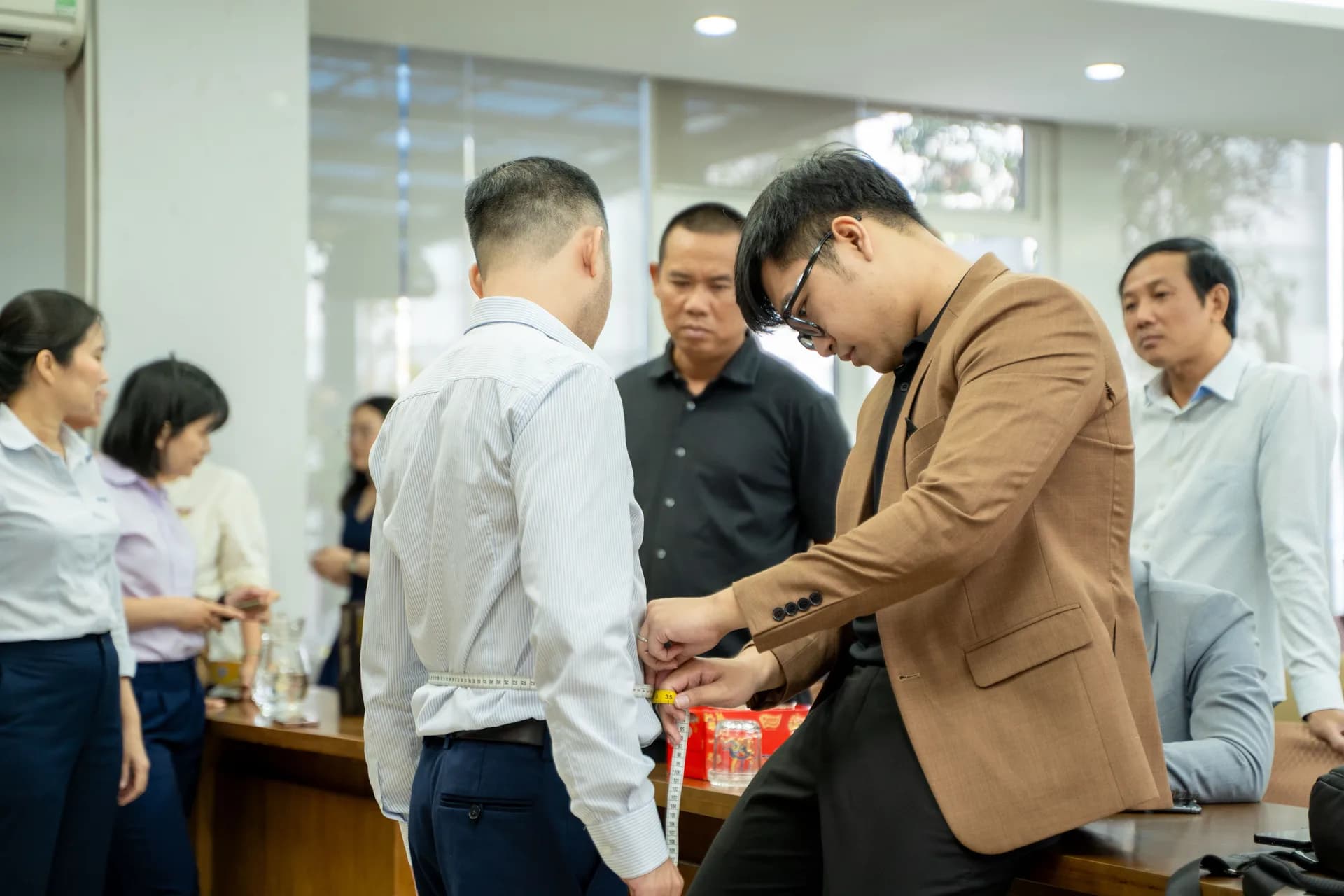 Đo vòng eo nhân viên nam giữa phòng họp, cán bộ công ty theo dõi