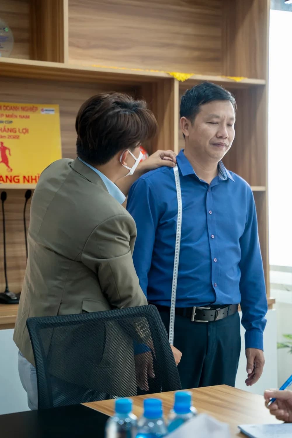 Đo ngang vai cho khách sơ mi xanh dương trong phòng họp, ảnh dọc ấm áp