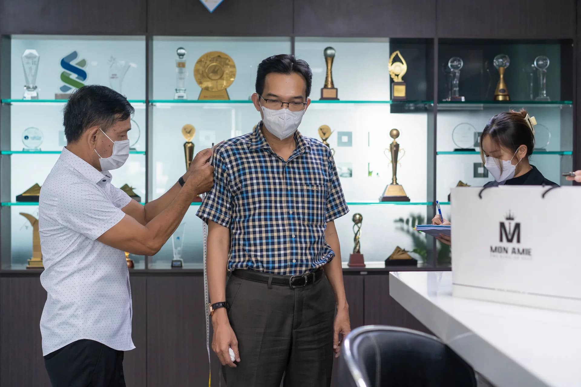 Đo vai cho cán bộ Hòa Bình cạnh tủ cúp lưu niệm