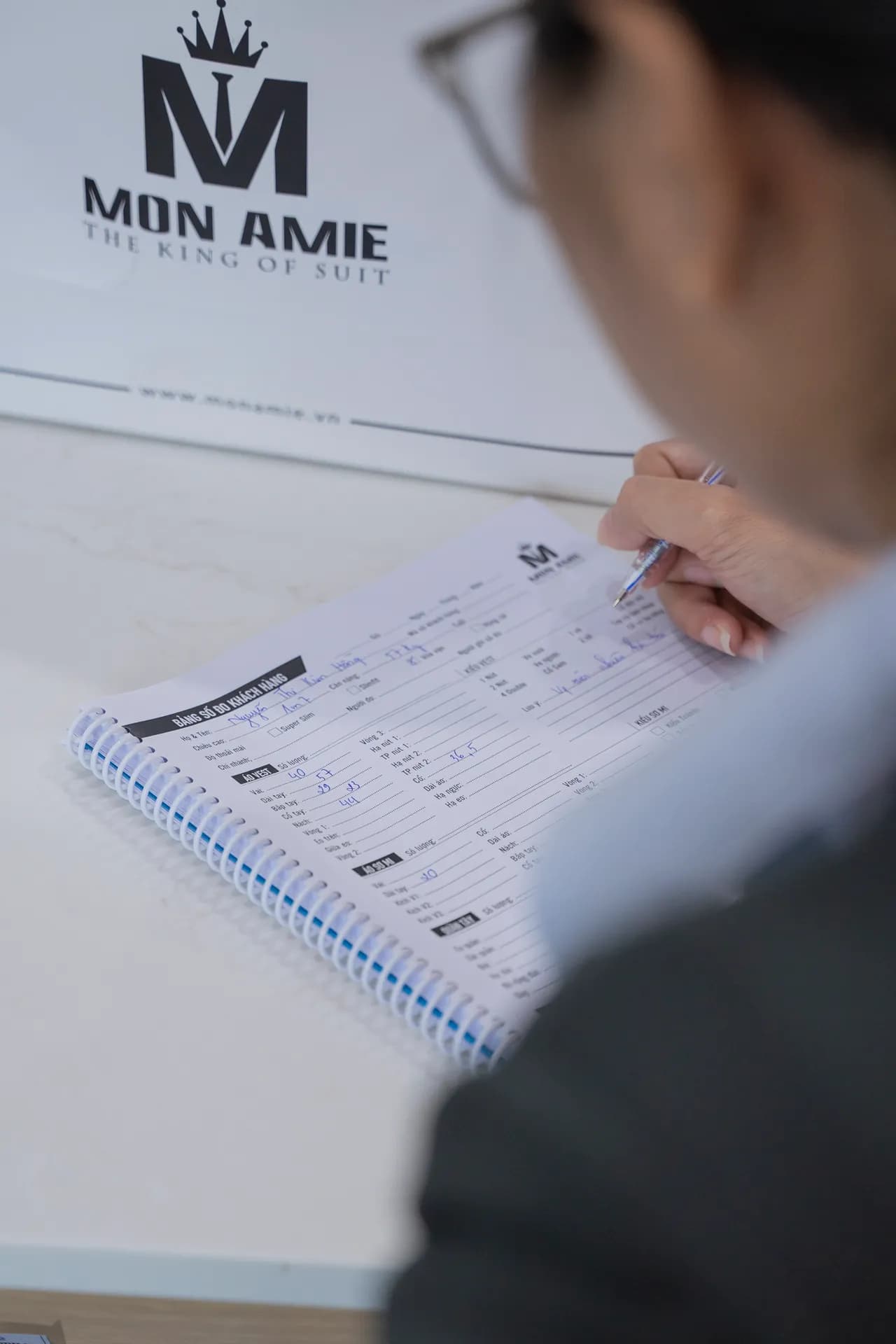 Phiếu số đo in logo Mon Amie đang được ghi chép khi đo may