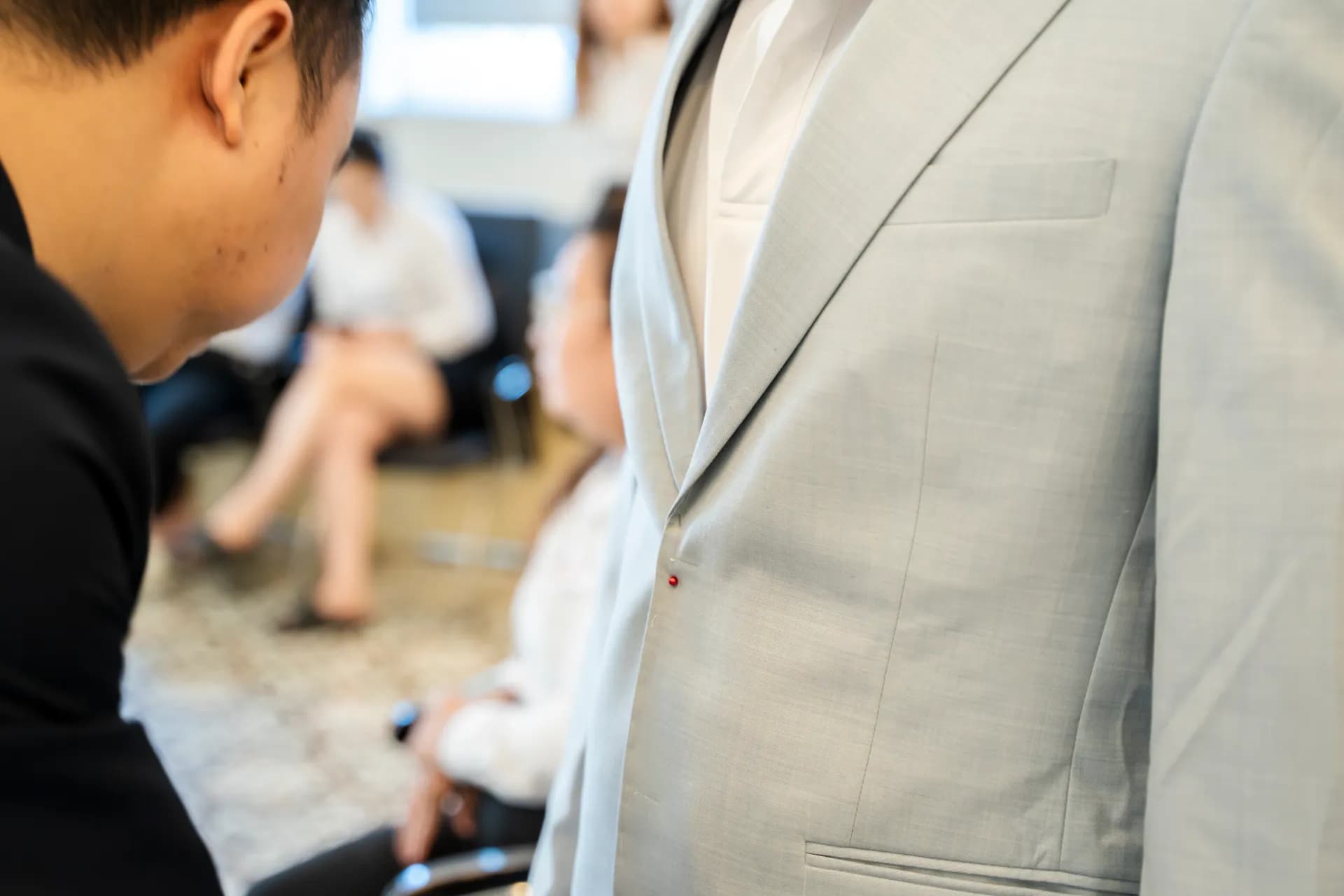 Cận cảnh ve áo suit xám nhạt có chỉ khuyết đỏ, thợ chỉnh sửa, nền mờ