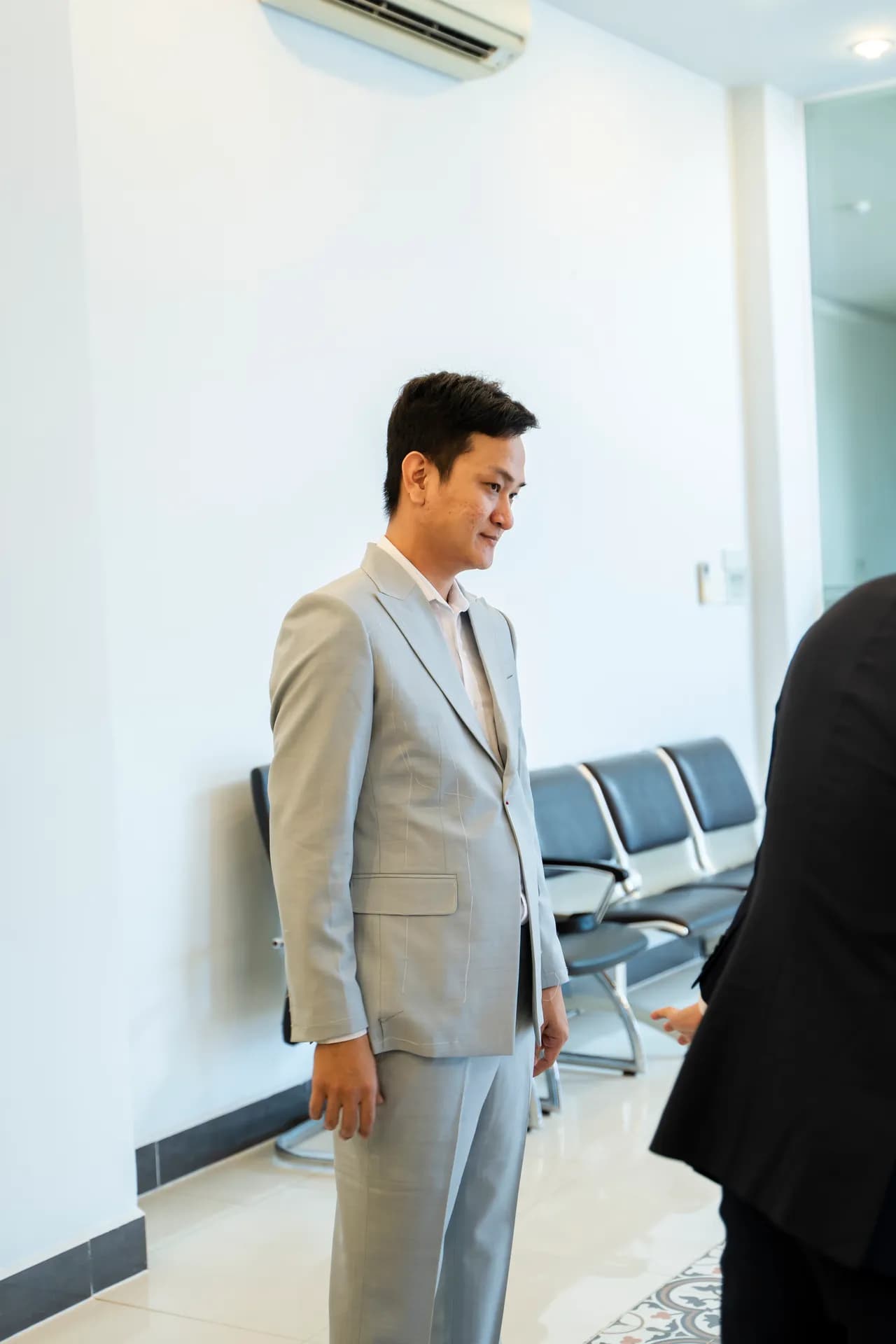 Khách thử suit xám nhạt, nhìn xuống chỉnh dáng áo trong sảnh sáng
