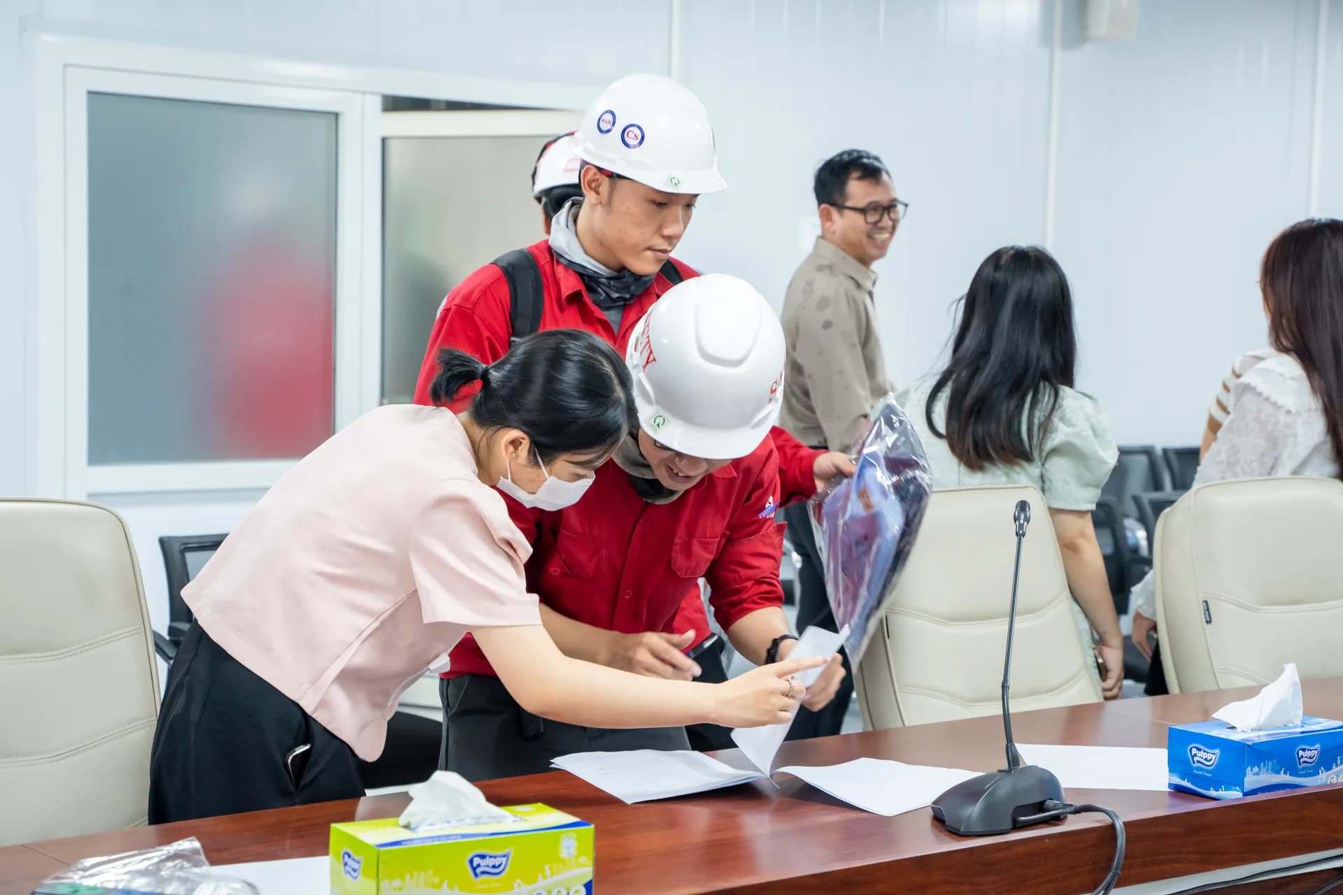 Công nhân kỹ thuật mũ bảo hộ đến nhận đồng phục, có nhân viên hướng dẫn ký nhận
