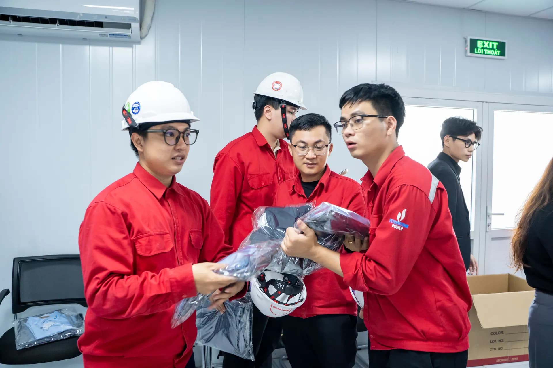 Nhân viên áo bảo hộ đỏ nhận bộ sơ mi đồng phục mới giao, cùng trao đổi vui vẻ