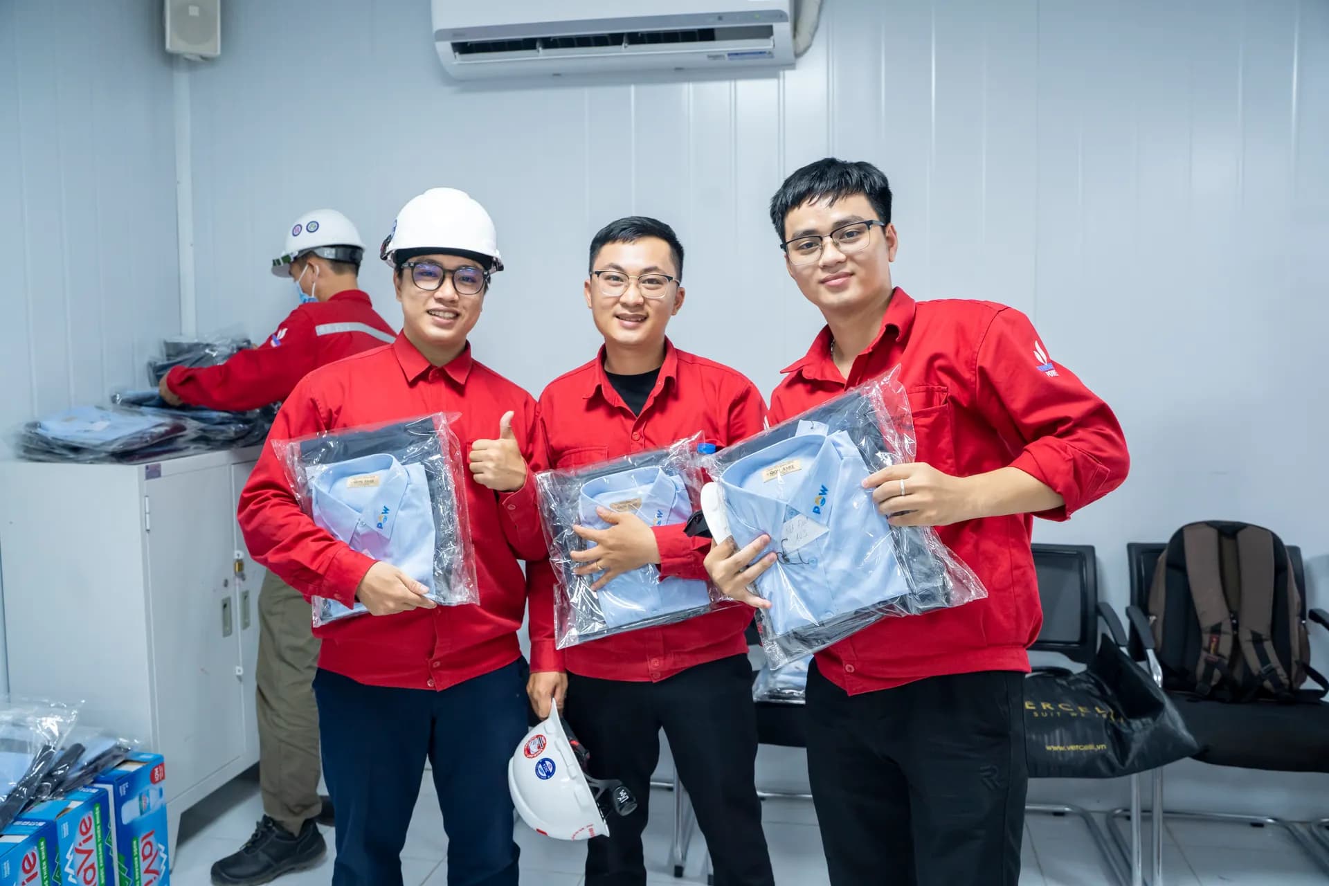 Ba nhân viên cười tươi giơ ngón cái, cầm những bộ sơ mi xanh nhạt vừa nhận