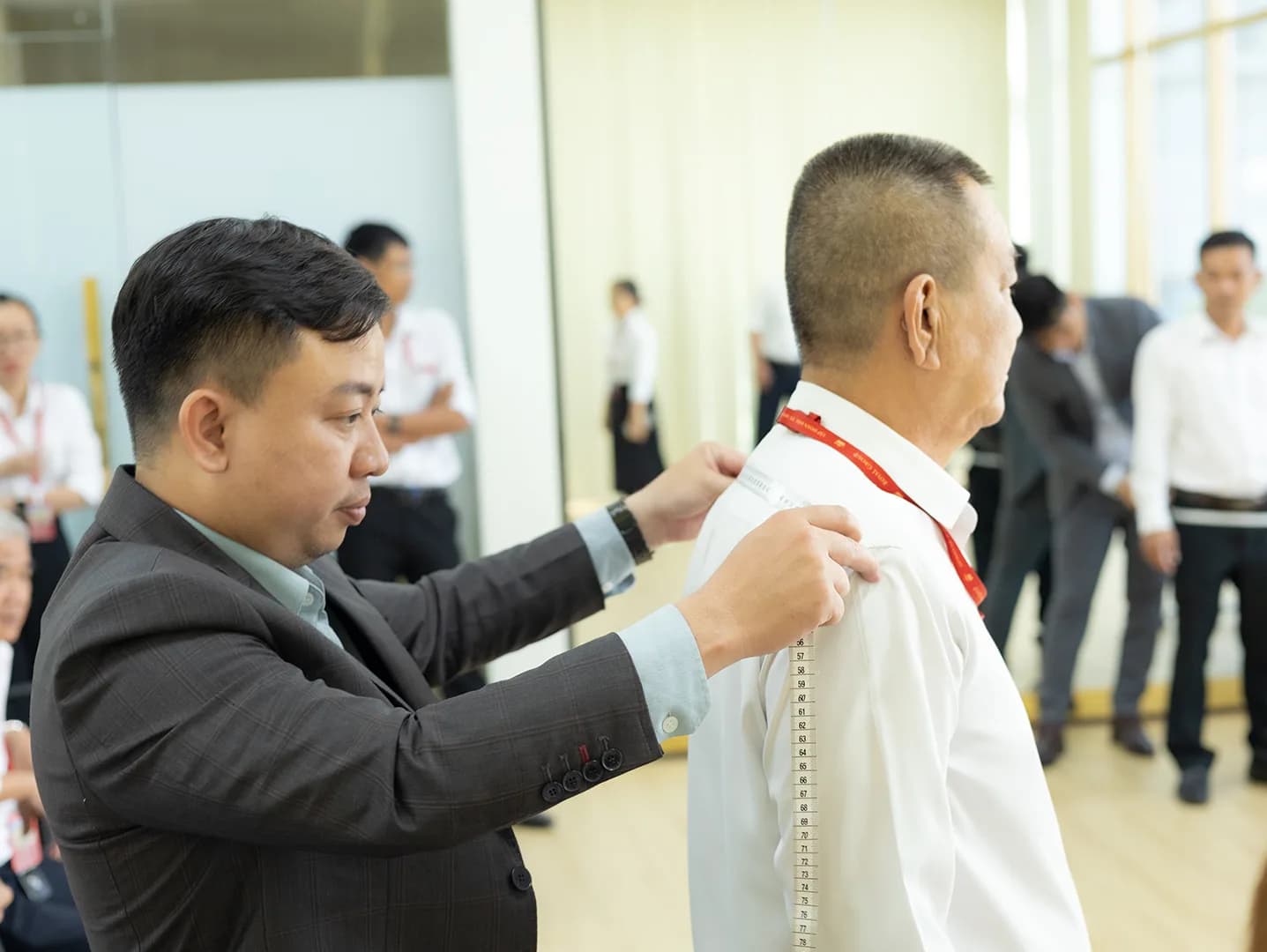 Đo dài vai cho nhân viên lớn tuổi, đồng nghiệp xếp hàng phía sau