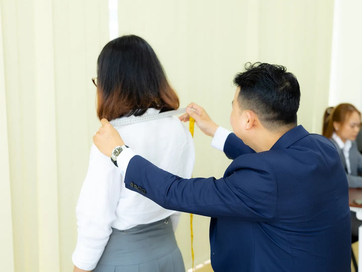 Đo ngang vai từ phía sau cho nữ nhân viên, thợ mặc blazer xanh navy