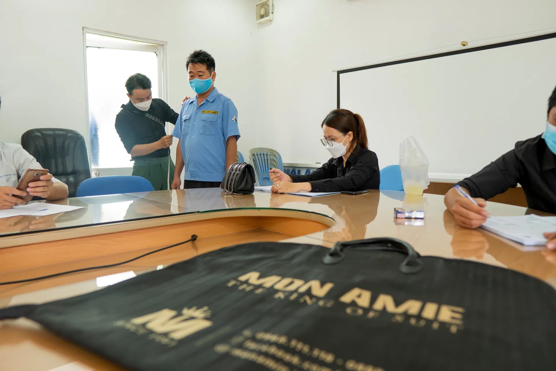 Đo số đo cho nhân viên đang mặc đồng phục cũ, túi Mon Amie đặt trên bàn
