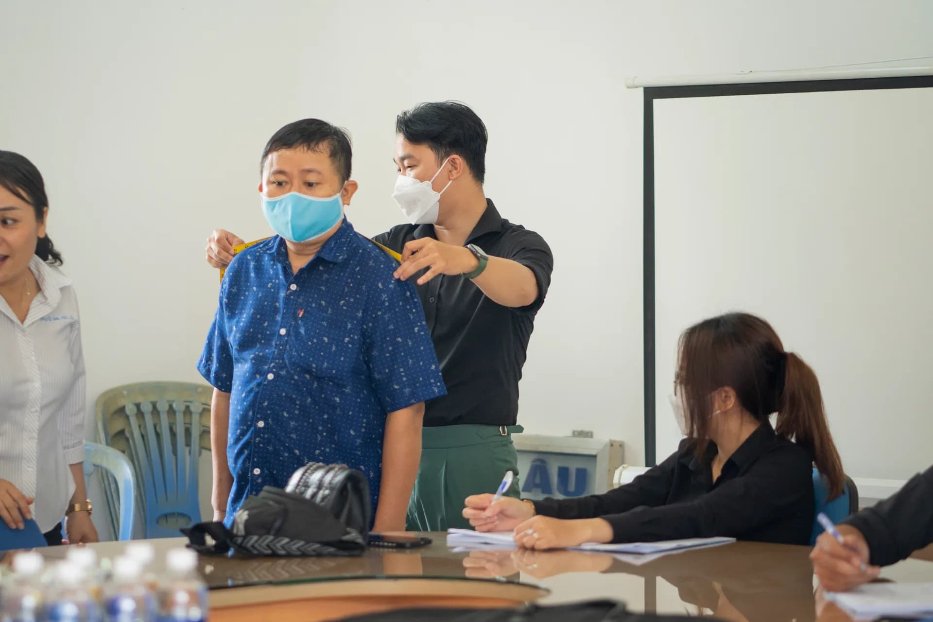 Đo vòng cổ và vai cho nhân viên áo xanh, phiếu số đo ghi chép ngay bên cạnh