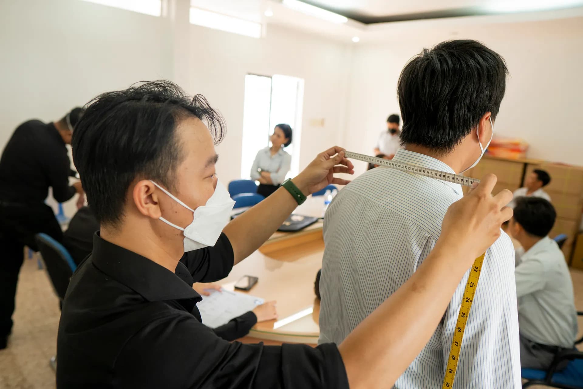Thợ đo ngang vai cho khách áo sơ mi sọc trong phòng họp sáng