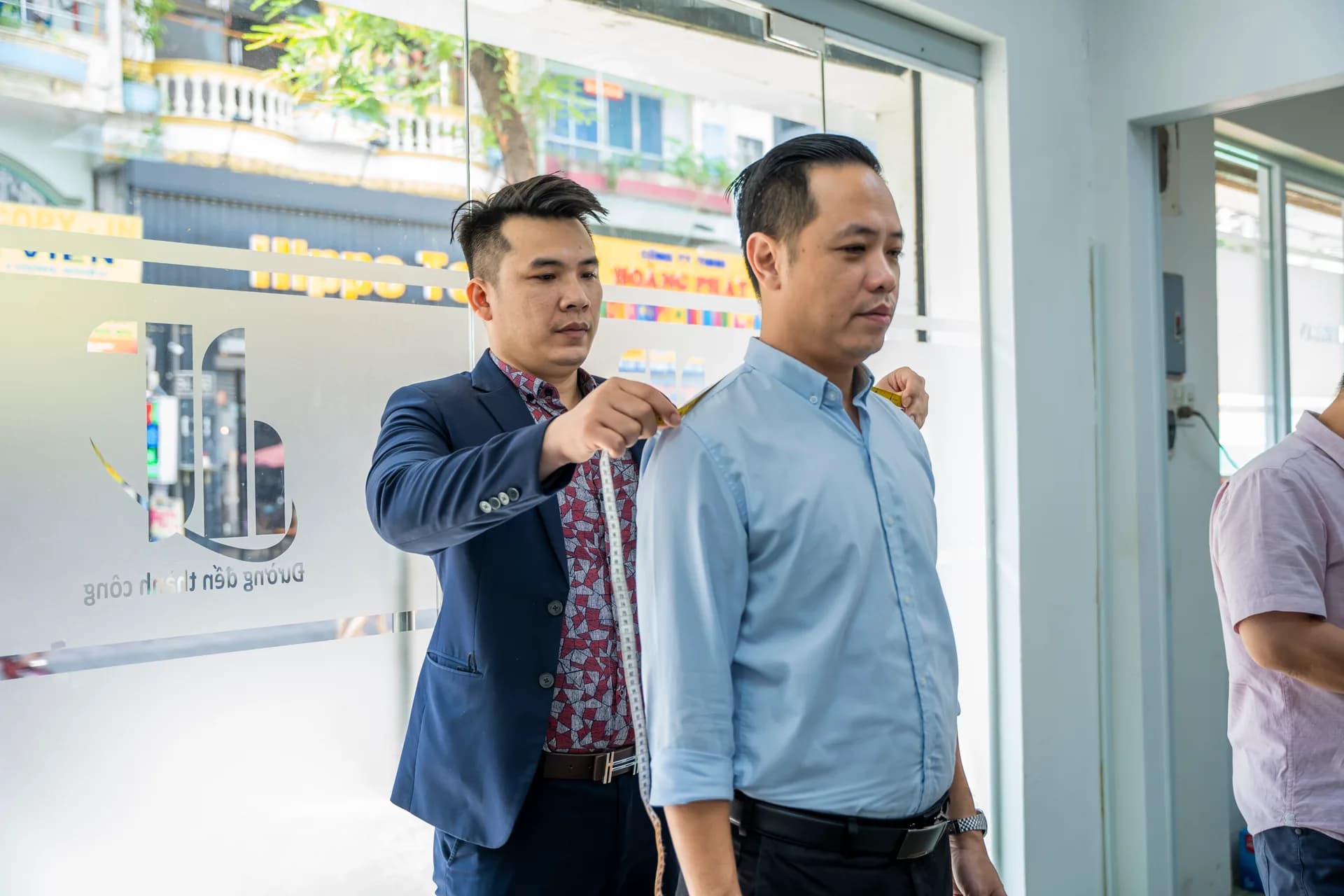 Đo vai cho nhân viên nam trước cửa kính có logo Viện