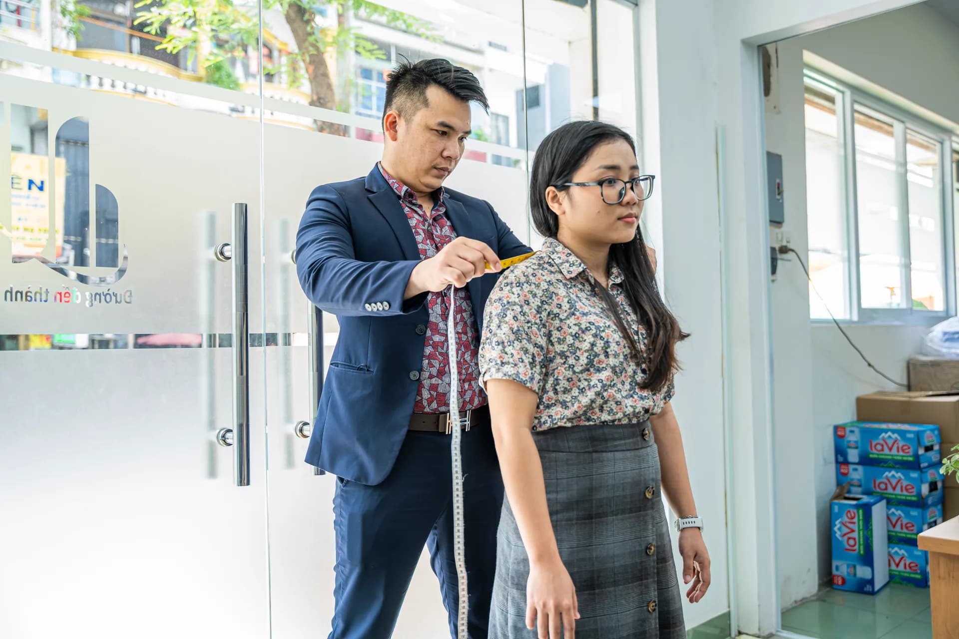 Đo dài áo cho nhân viên nữ trước cửa kính công ty