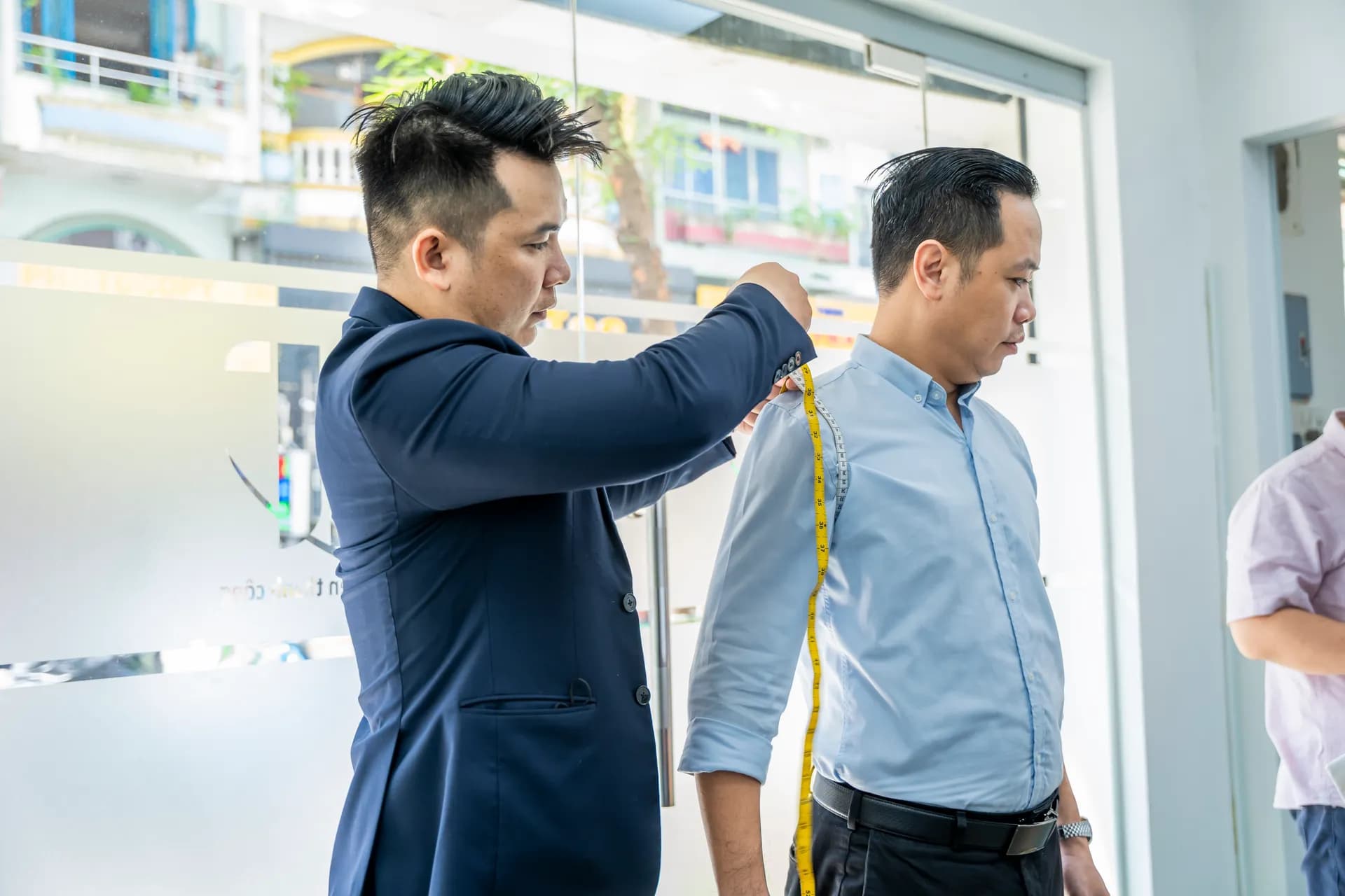 Đo chiều dài tay áo cho khách sơ mi xanh nhạt, thước dây vàng nổi bật