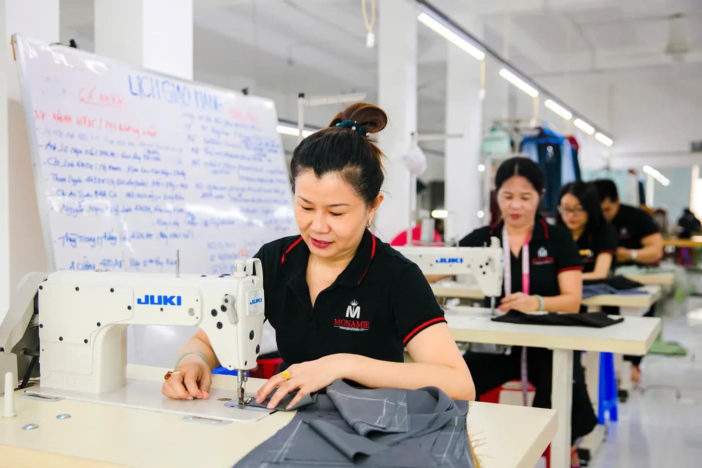 Dãy nữ thợ áo polo đen đồng phục may vest bên bảng lịch giao