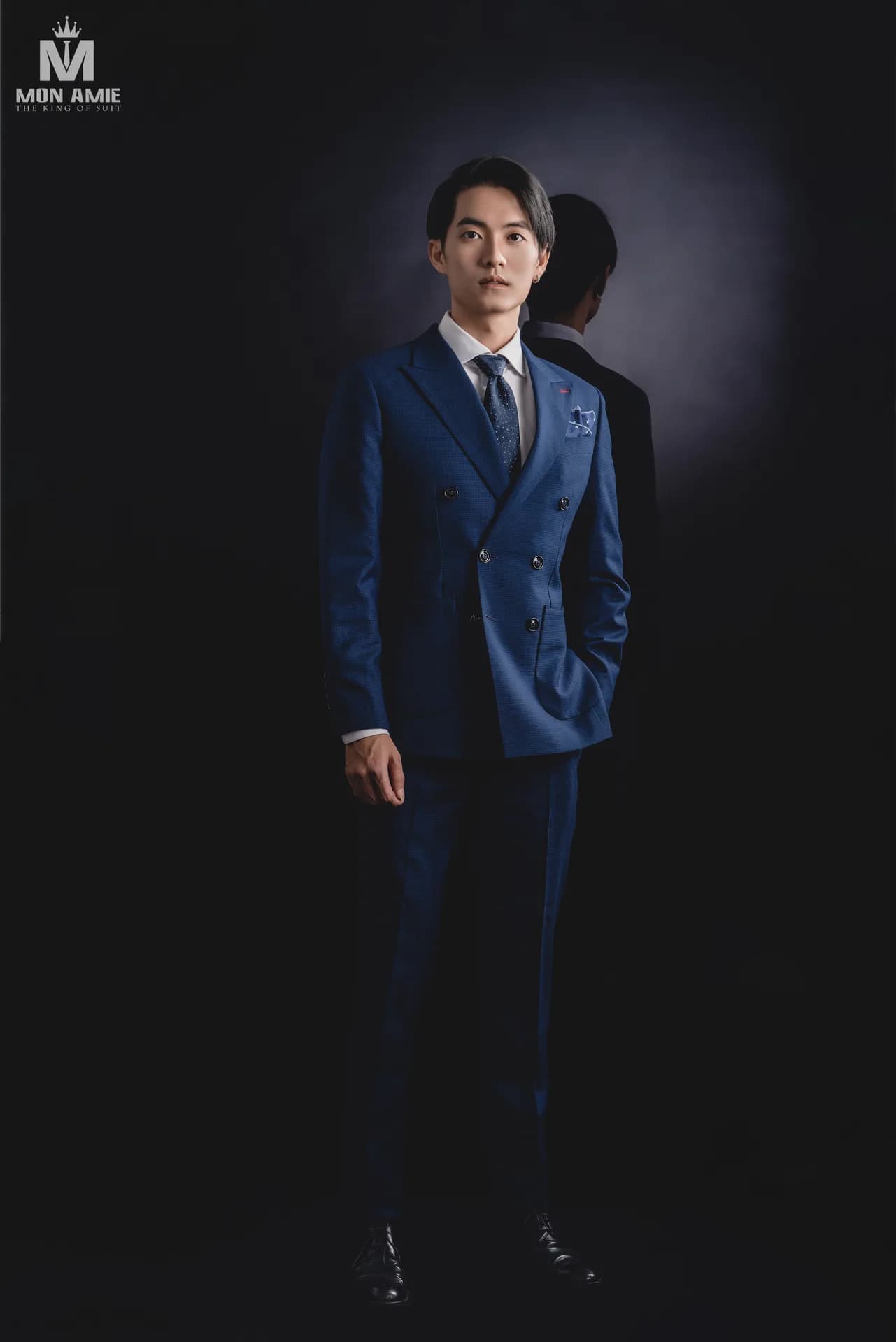 Suit kẻ ô xám phối gilet, bên giá treo suit và phụ kiện trong atelier