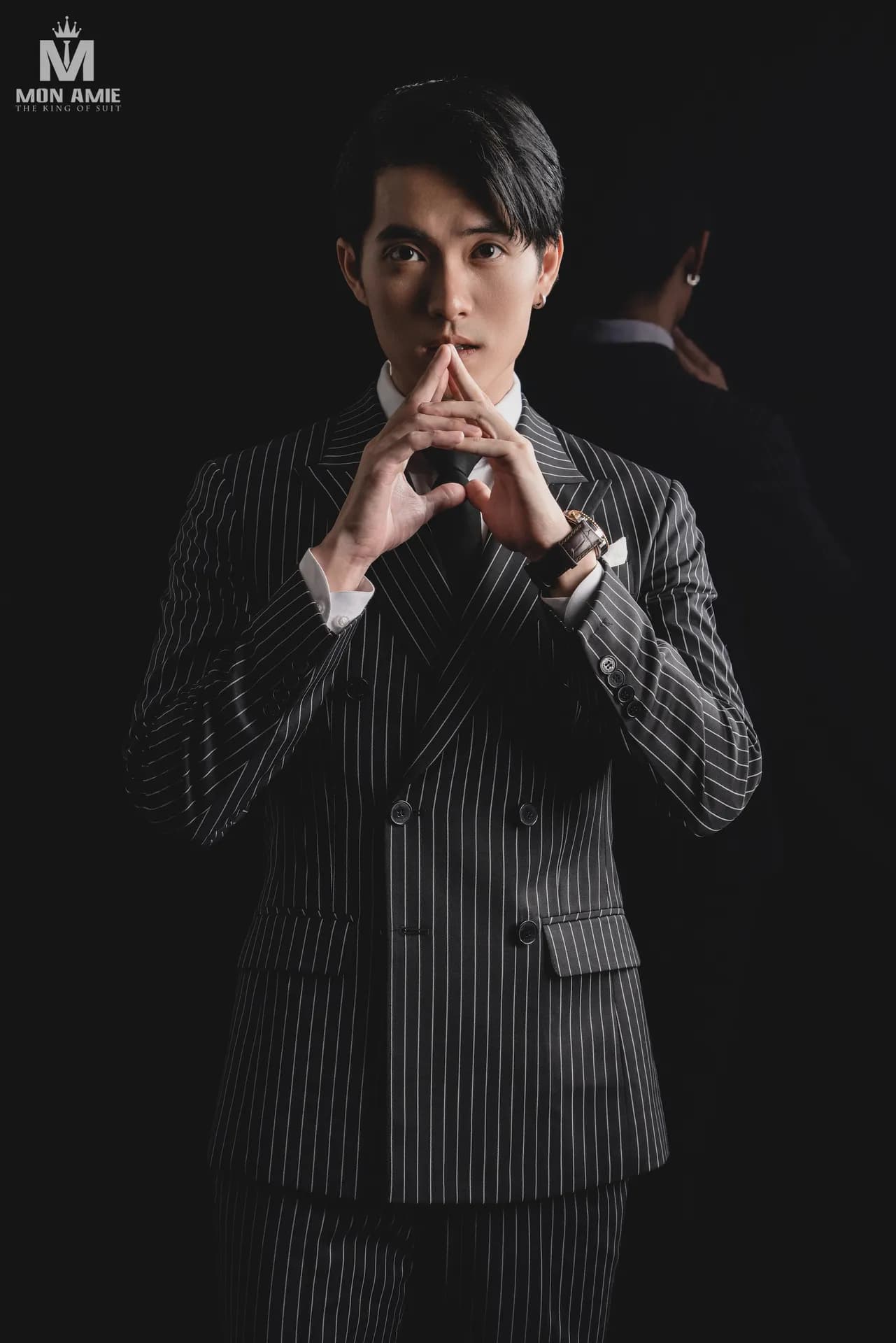Vest sọc xám hai hàng khuy, hai tay chắp trước mặt trong studio tối