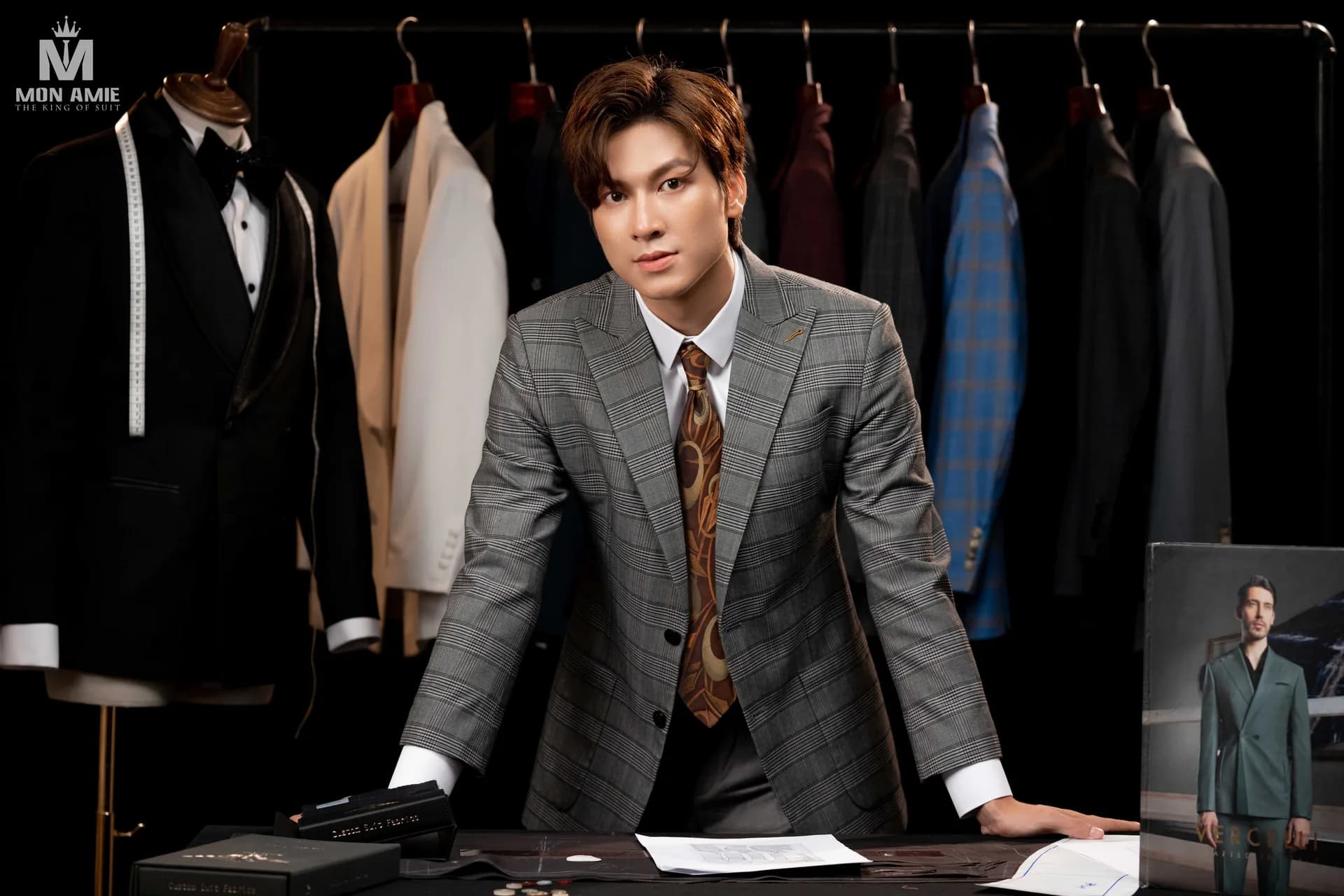 Suit caro xám và ánh nhìn thẳng, nền xưởng may tối màu
