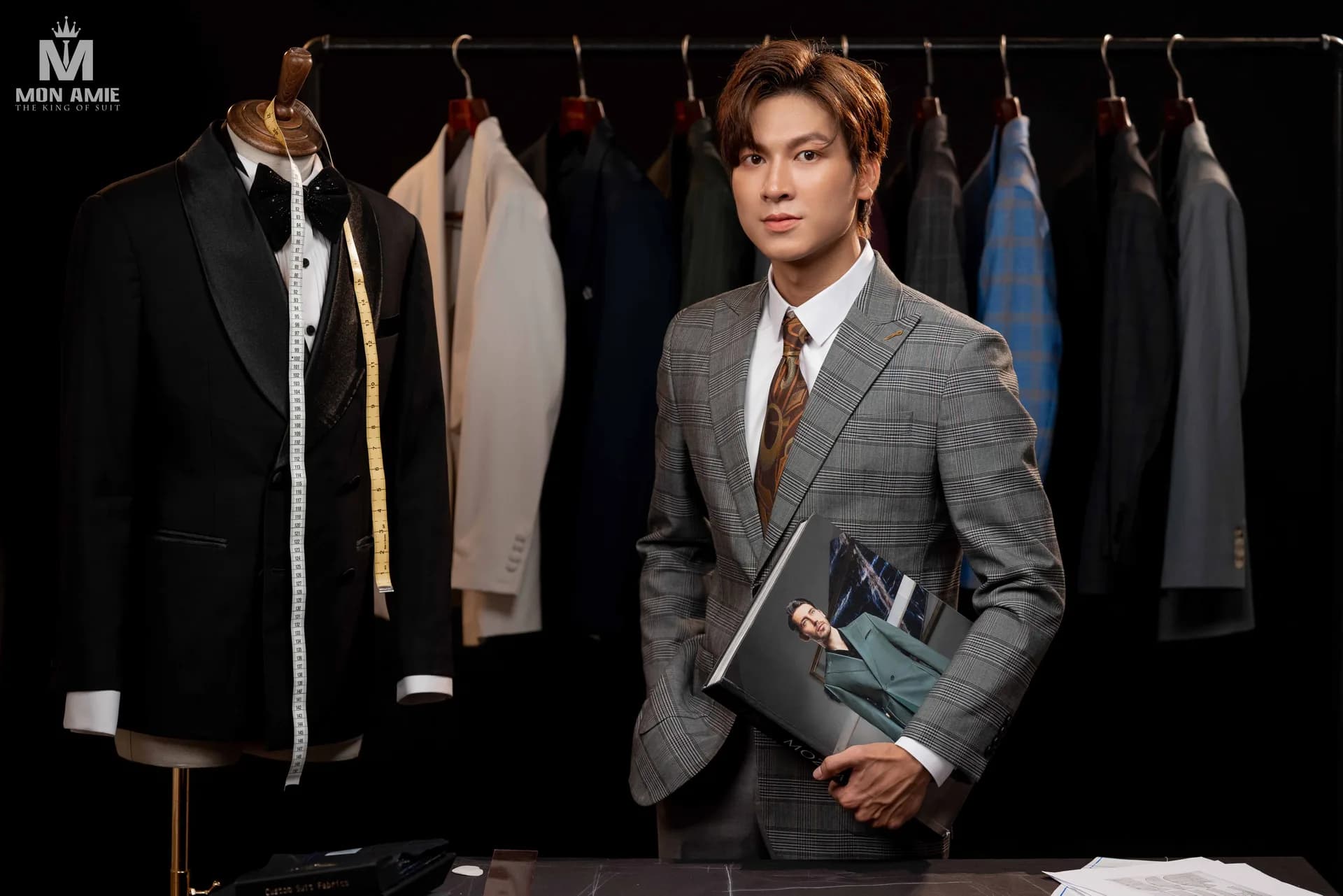 Ôm cuốn catalogue vải cạnh mannequin tuxedo