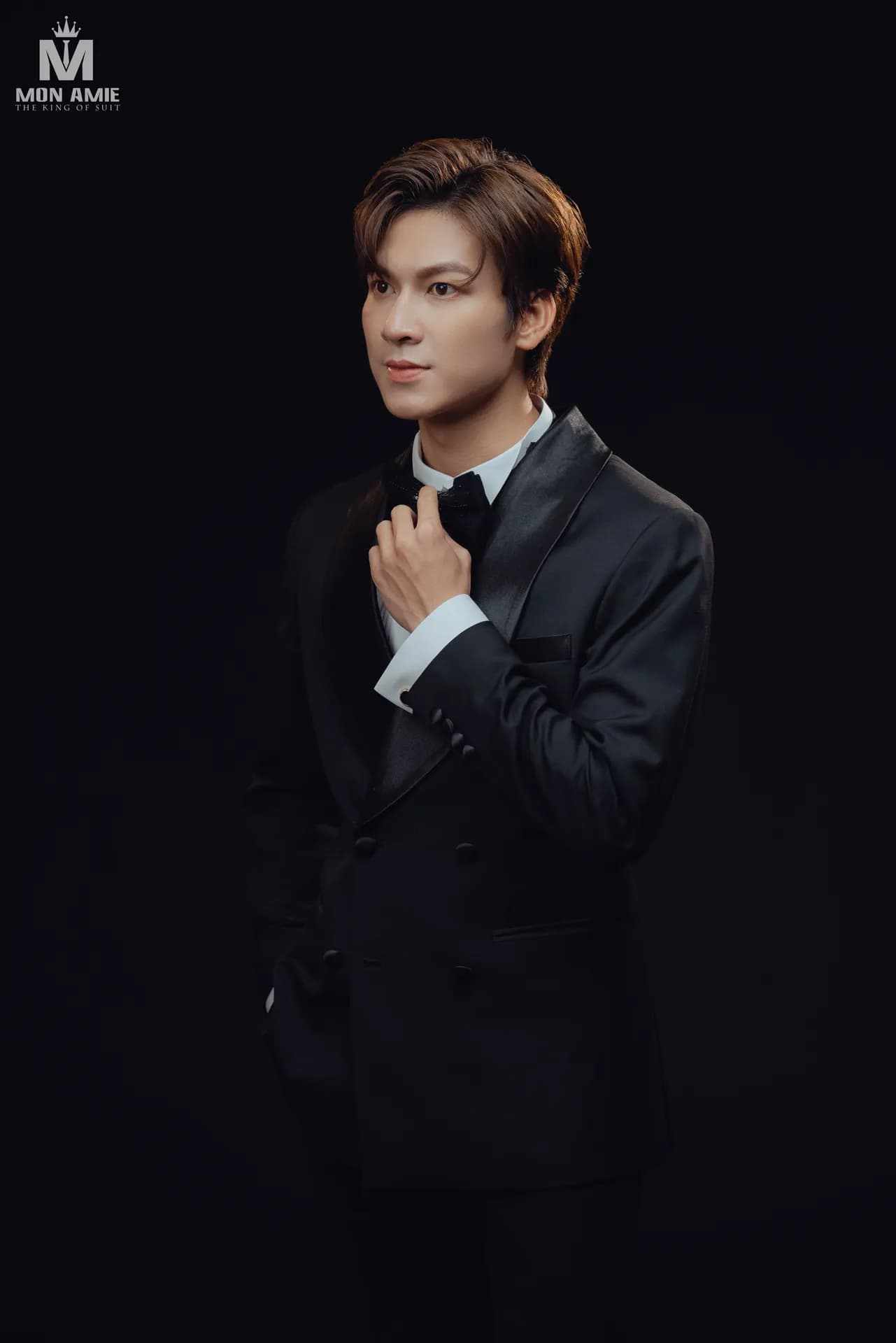 Tuxedo đen cổ lụa hai hàng khuy, nơ đen, nền studio tối