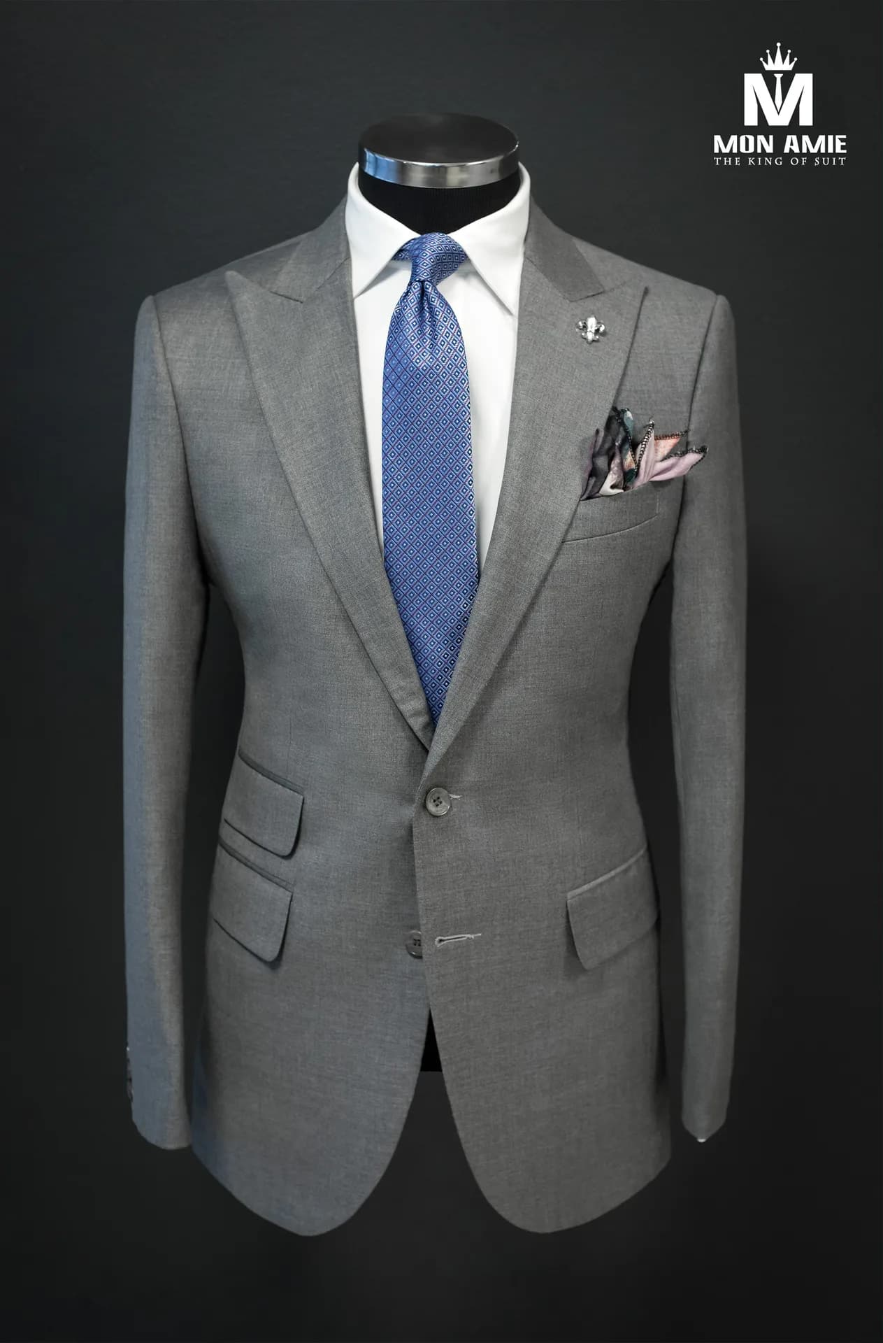 Suit xám ve nhọn trên ma-nơ-canh, cà vạt xanh và ghim cài áo