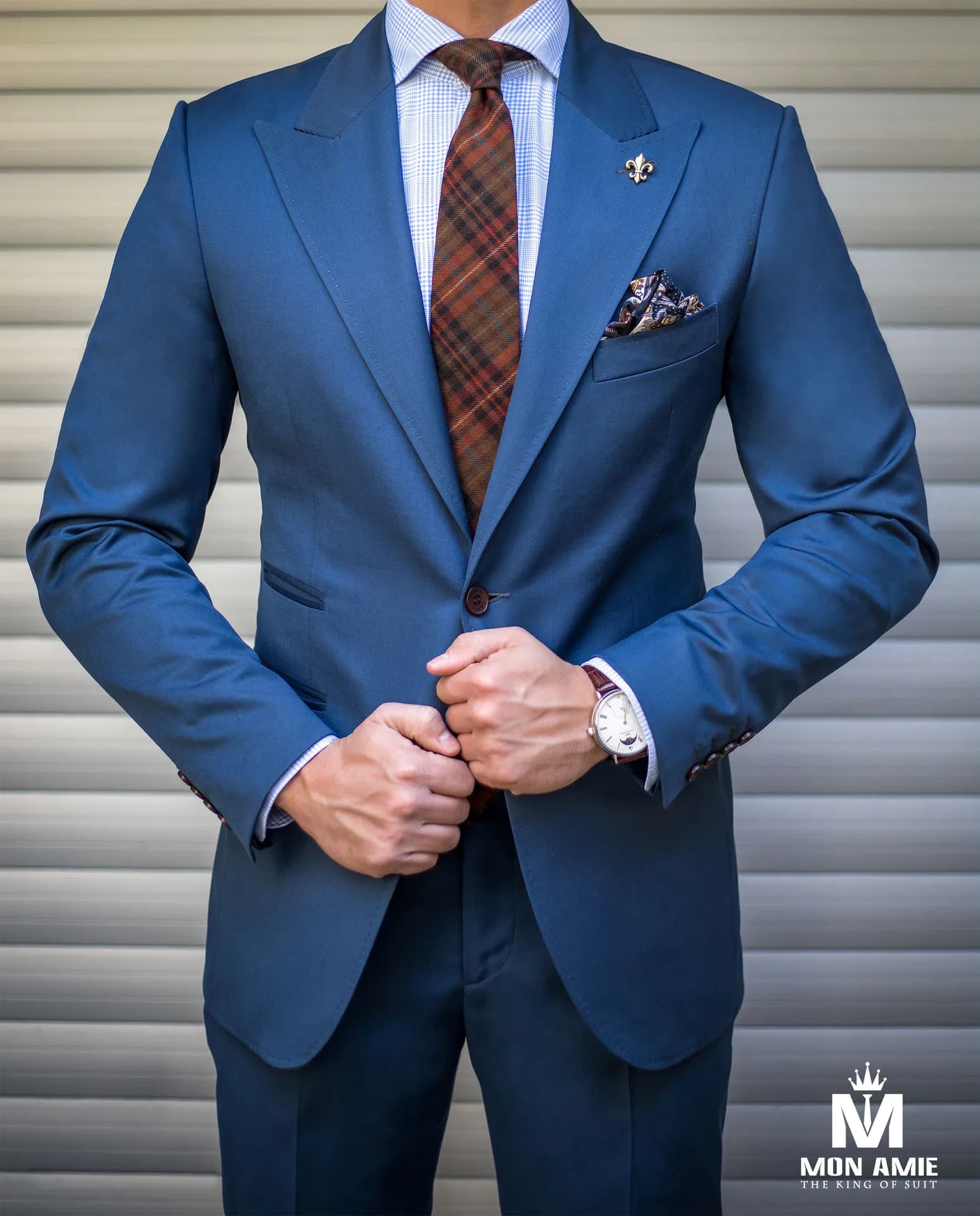 Suit xanh dương ve nhọn, cà vạt kẻ ô nâu đỏ, khăn cài túi, cận thân