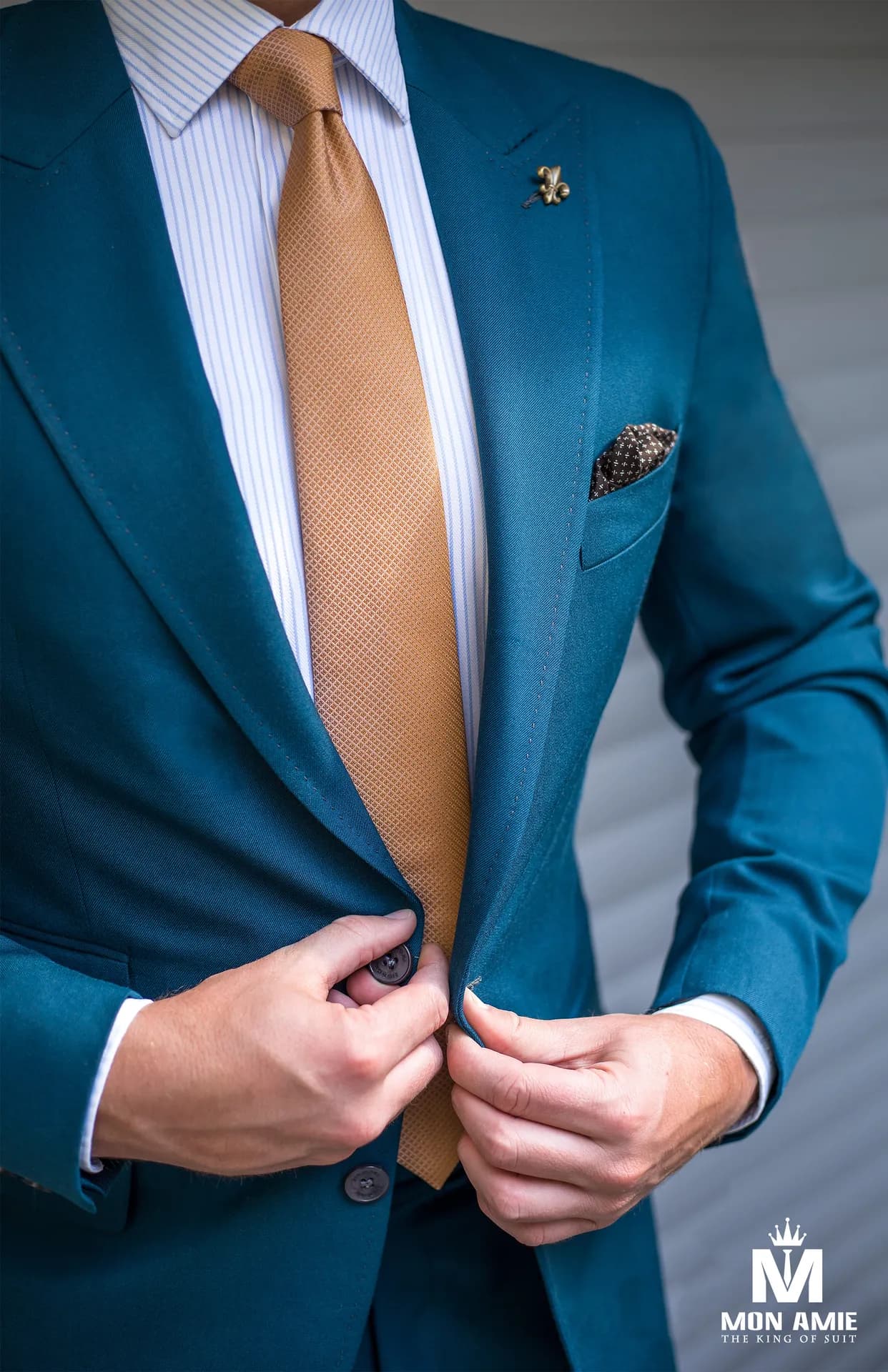 Suit xanh petrol cận cảnh, cà vạt vàng đồng, tay cài khuy áo