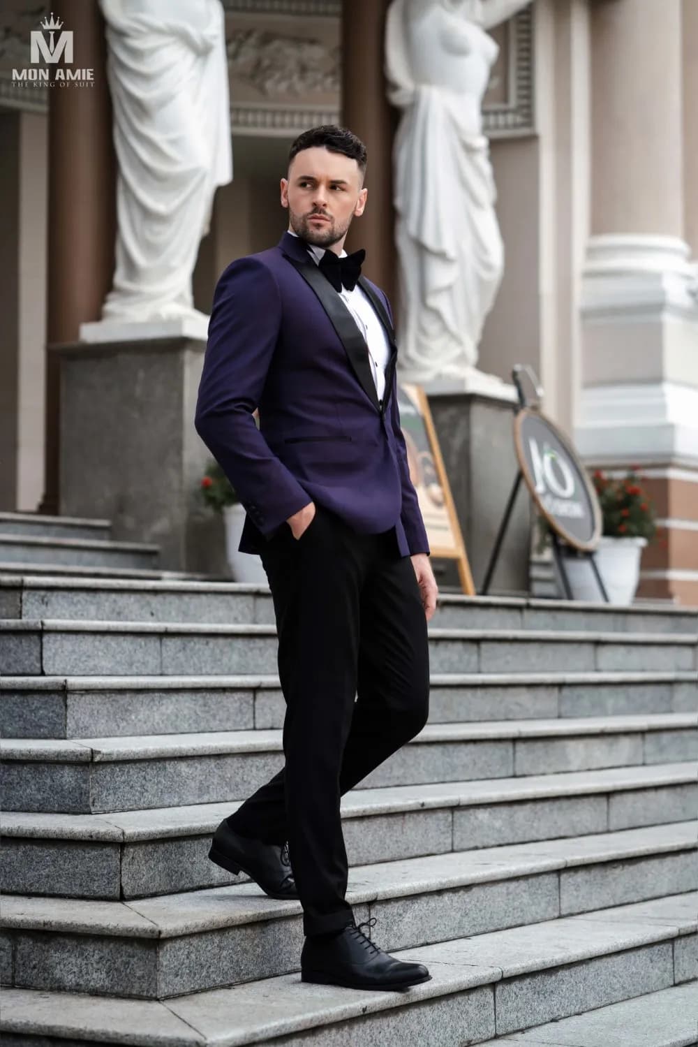Tuxedo tím than, nơ đen, bước xuống bậc thềm đá trước toà nhà cổ