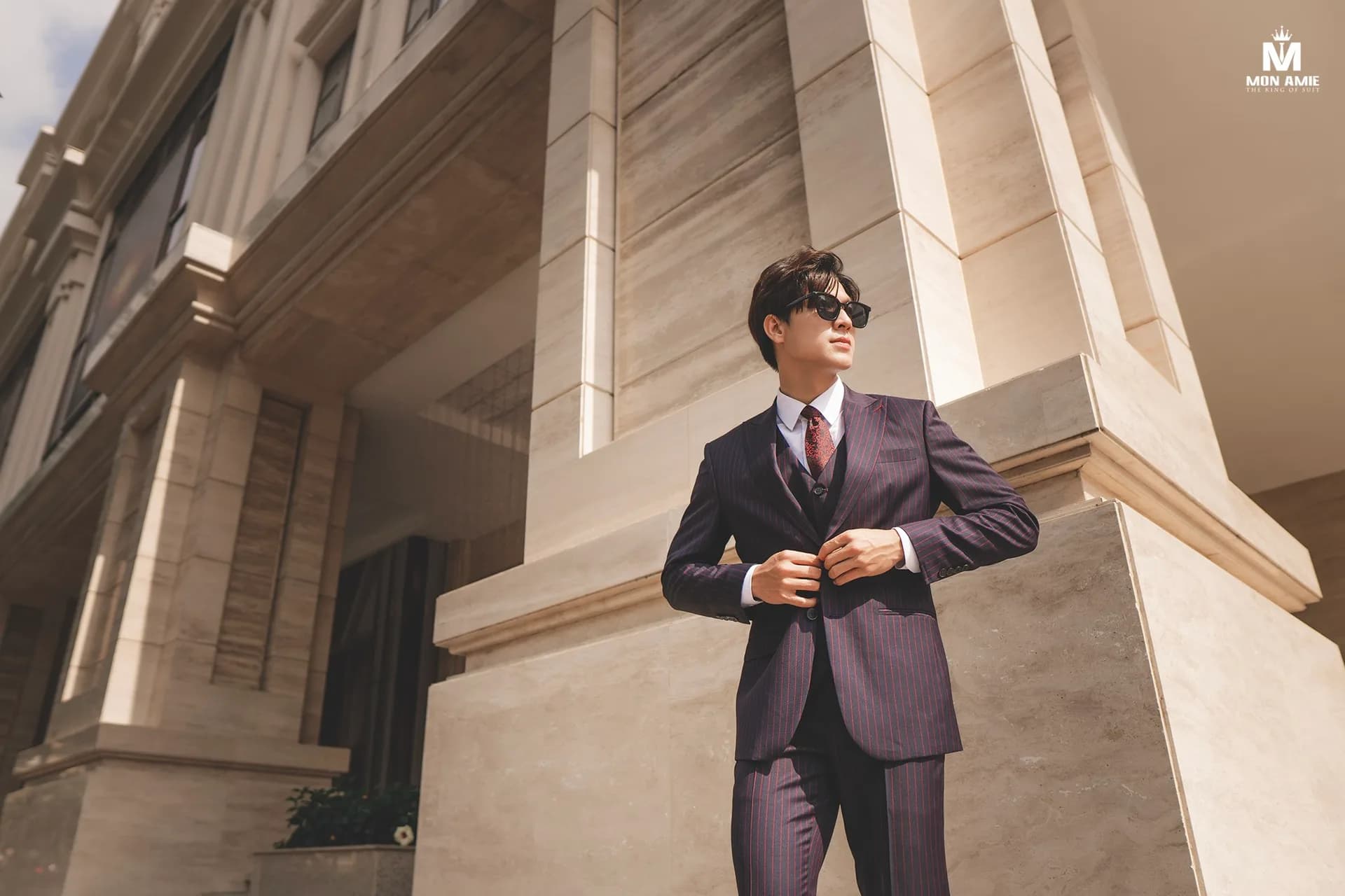 Suit ghi xám hai khuy, tay đưa lên chỉnh cà vạt kẻ nhỏ