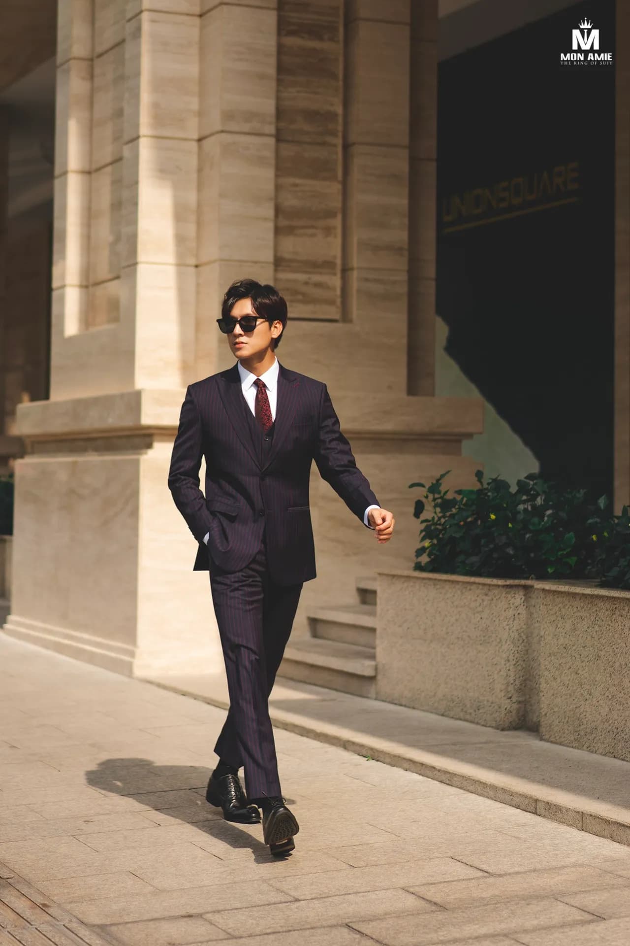 Suit nâu tím than ba mảnh sải bước dưới hàng cột đá sáng