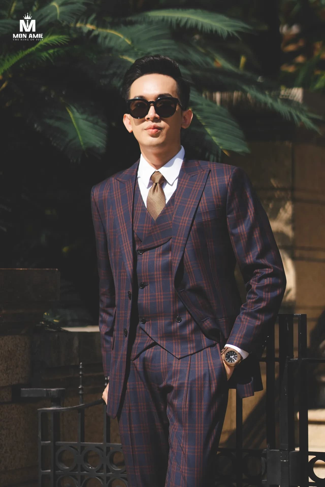 Suit ba mảnh caro xanh navy sọc nâu đỏ, kính râm và đồng hồ vàng hồng giữa nắng