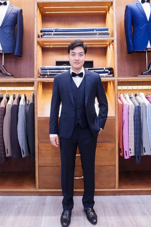 Suit ba mảnh xanh navy đậm nơ đen, sang trọng trước kệ vải gỗ