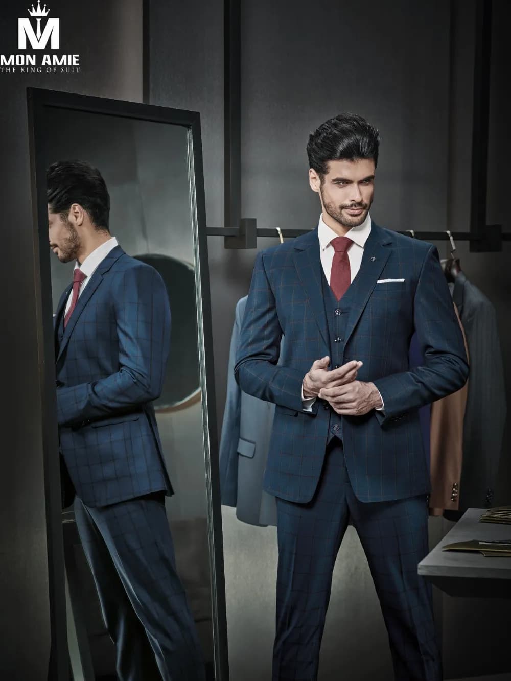 Suit ba mảnh navy kẻ ô, cà vạt đỏ đô, chỉnh tay áo trước gương
