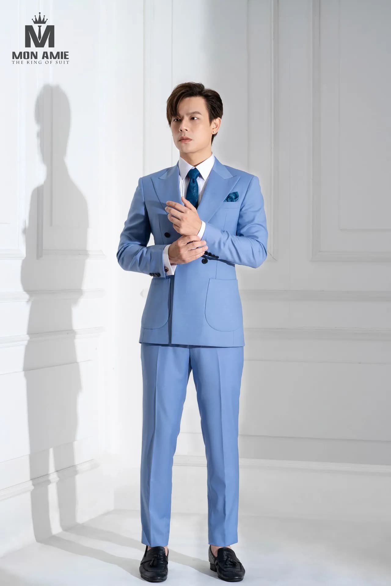 Suit xanh da trời hai hàng, cà vạt xanh, chỉnh măng sét trước tường trắng