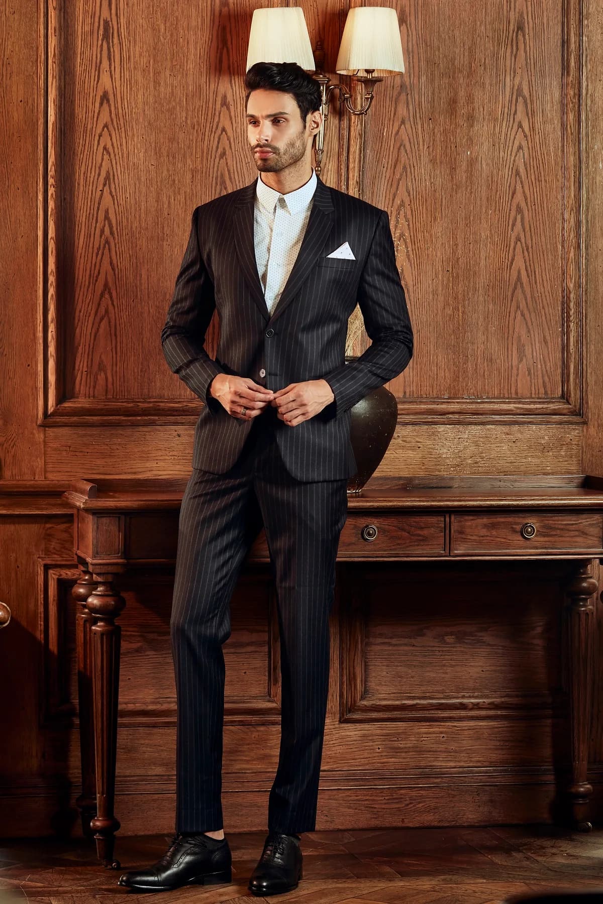 Suit sọc kim đen than, sơ mi chấm bi và khăn túi trắng bên bàn gỗ sồi