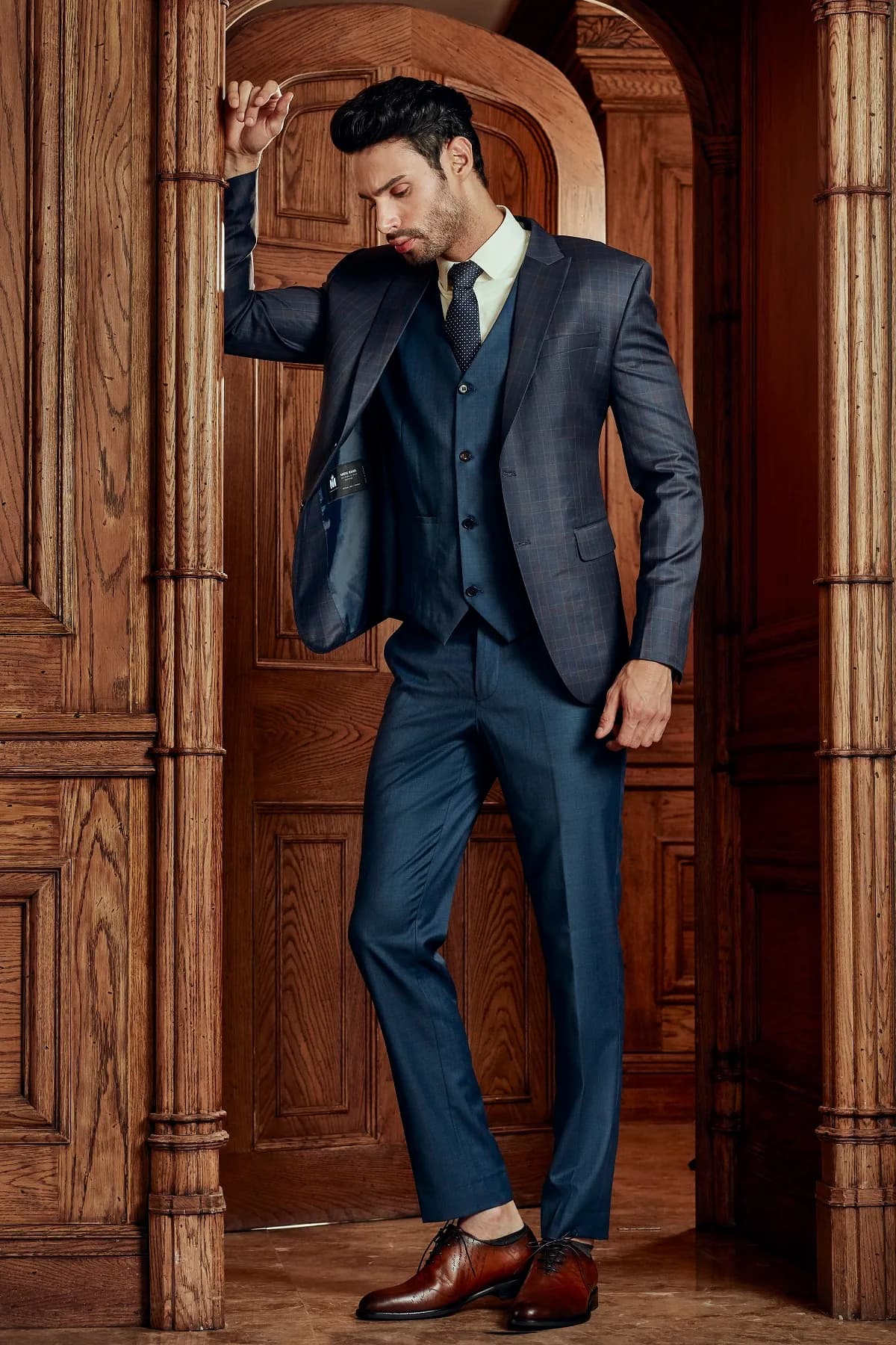 Suit ba mảnh xanh navy kẻ chìm, dáng tựa khung cửa gỗ đầy phong cách