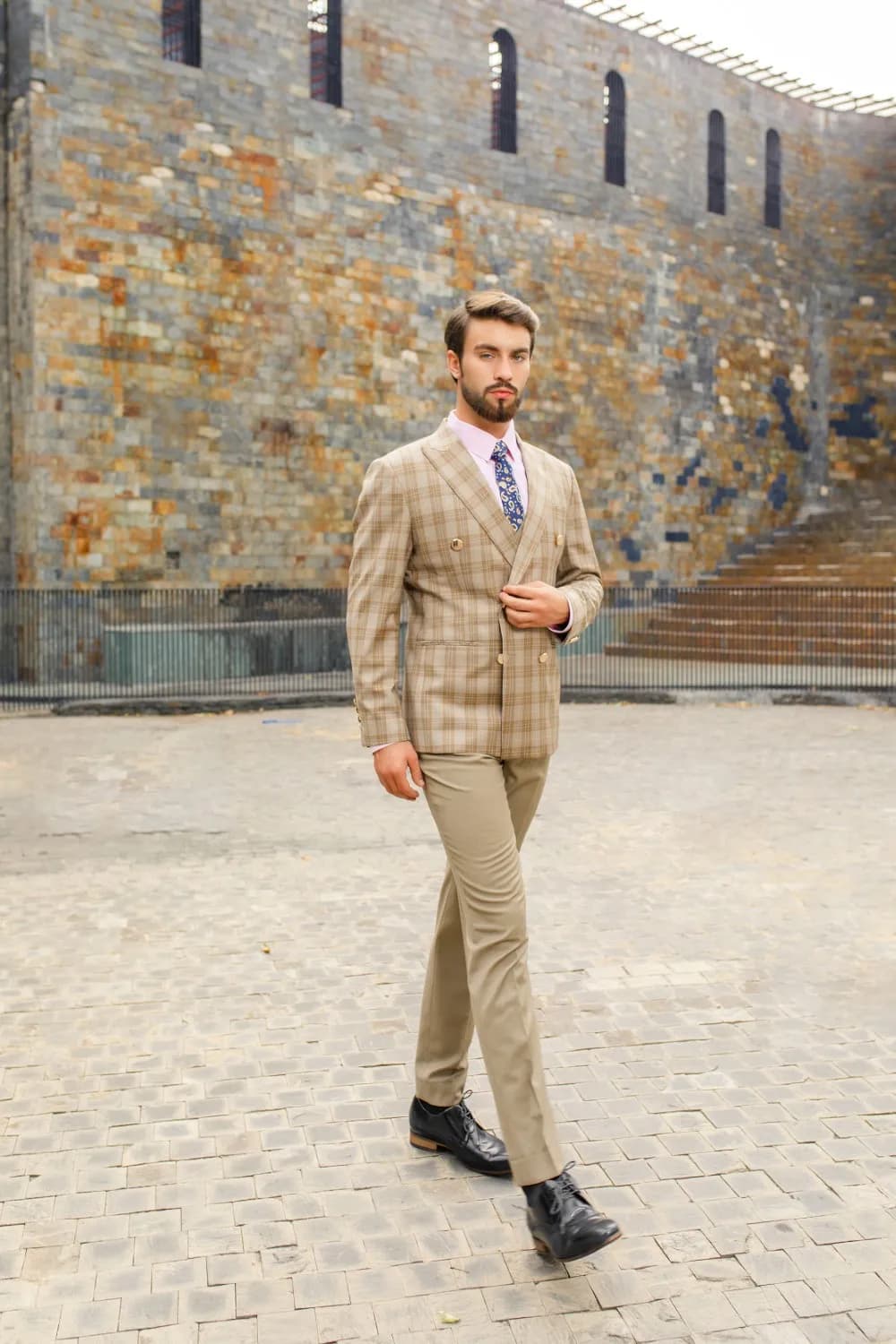 Suit be caro hai hàng khuy bước đi giữa sân đá, nền tường gạch cổ
